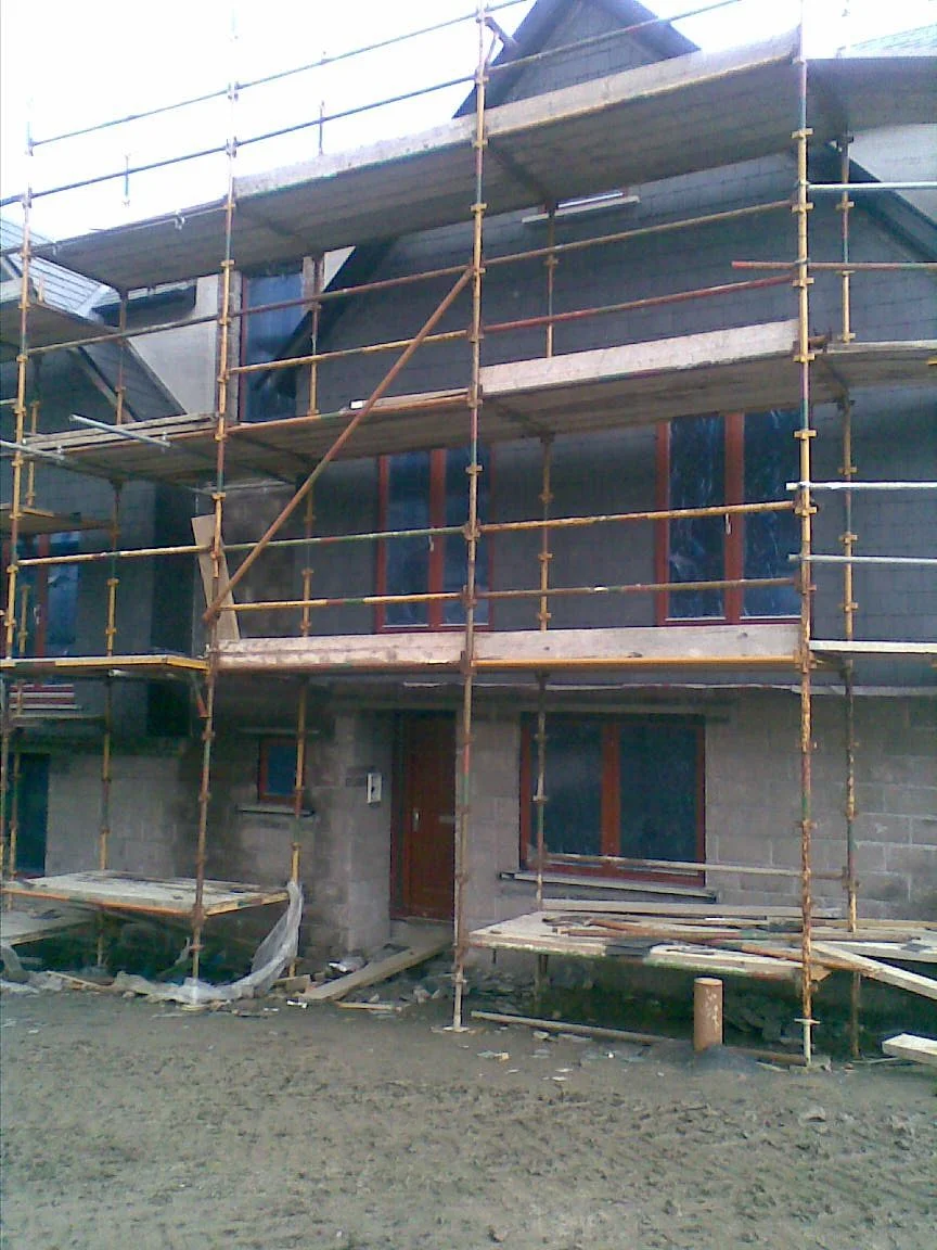 Scaffolding set up around a partially constructed building with unfinished walls and windows.
