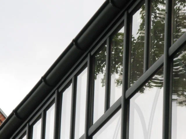 Close-up of a modern glass building facade with trees reflected in the windows.