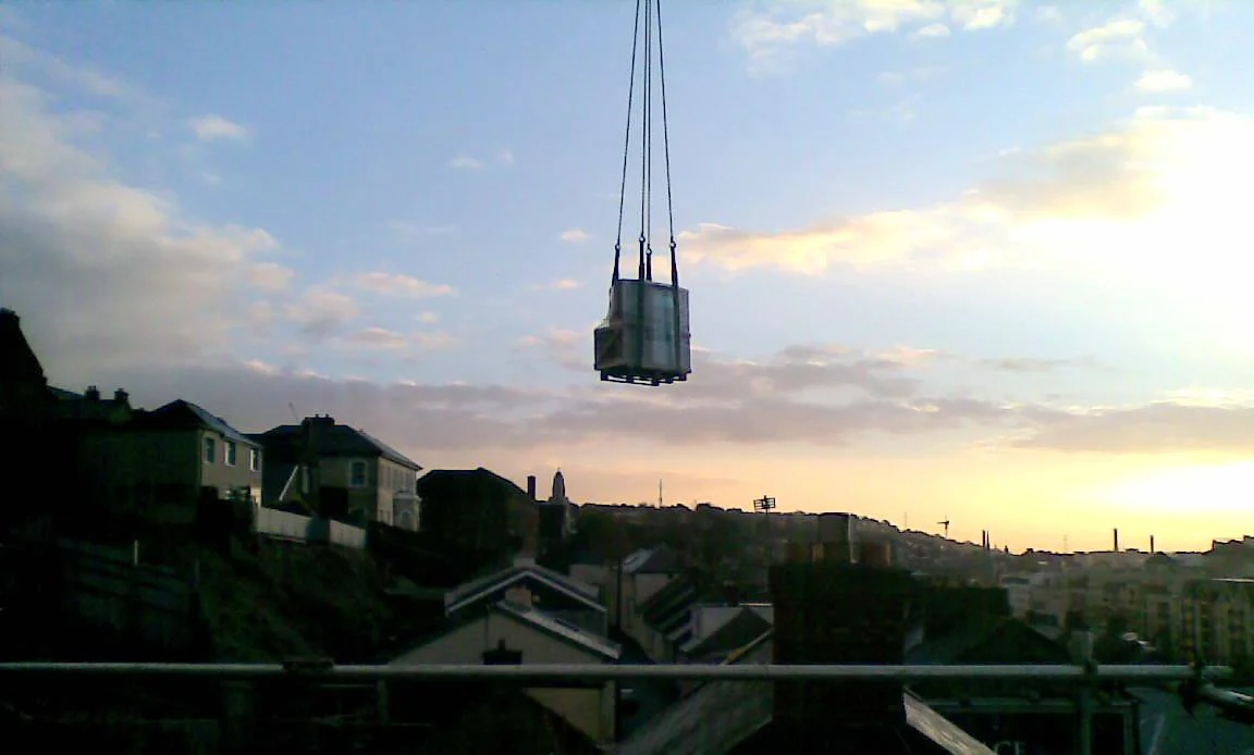 Shipping container being lifted by a crane over a residential area at sunset.