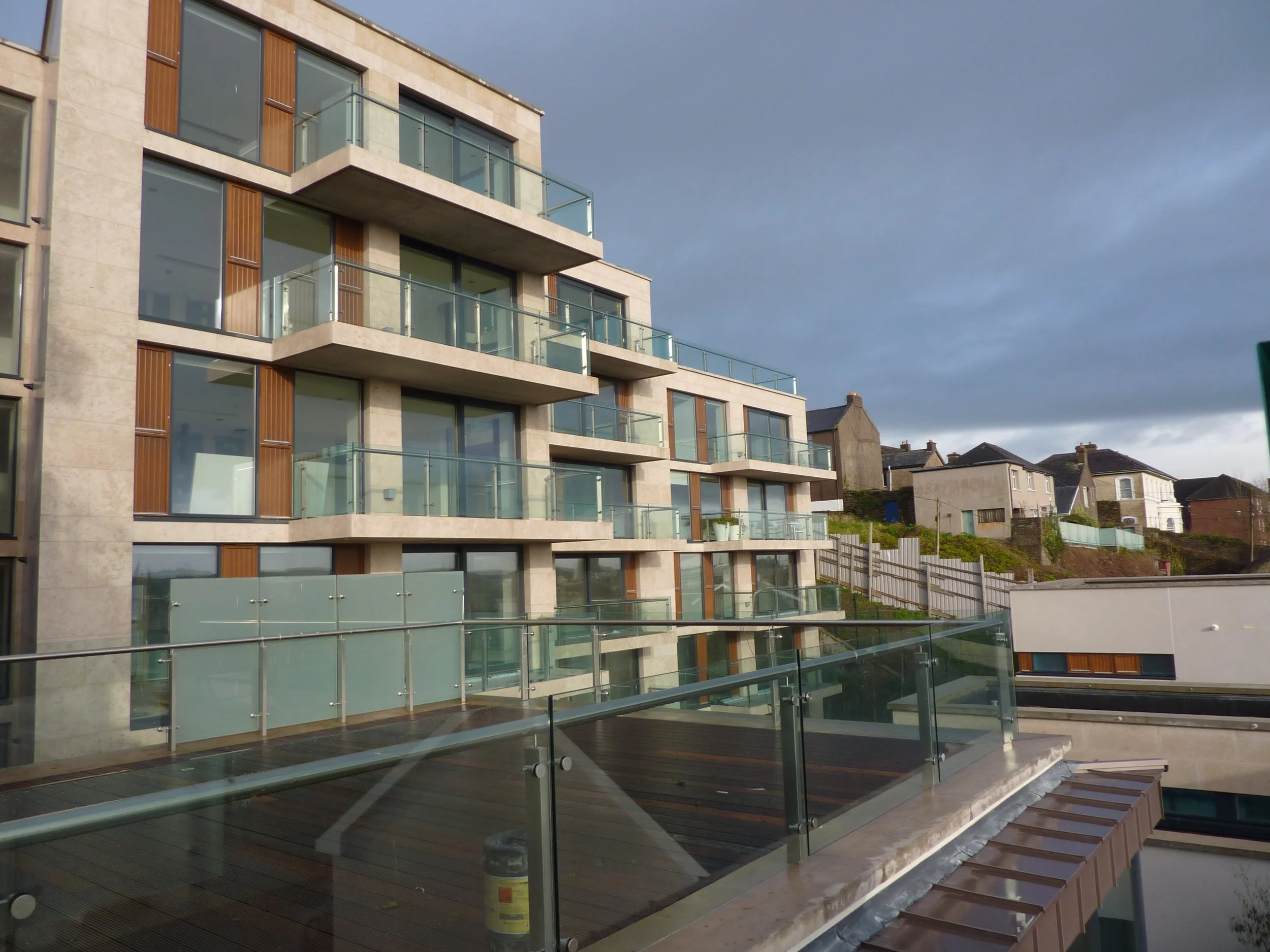 Modern apartment building with glass balconies and wooden accents against a cloudy sky.