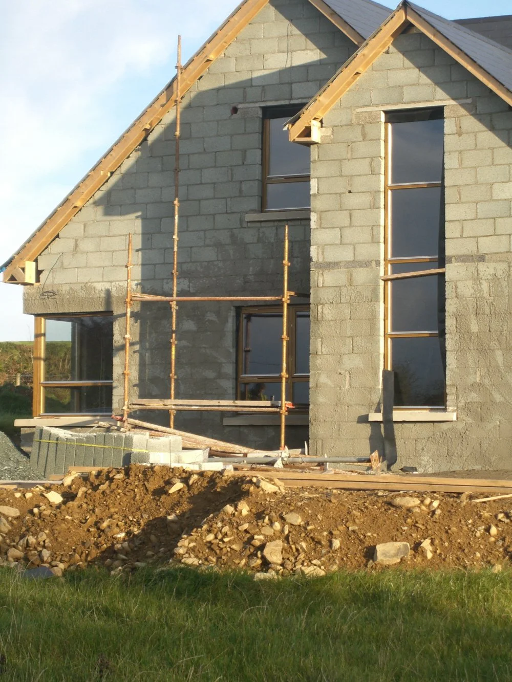 Partially constructed house with exposed concrete blocks, wooden scaffolding, and unpainted walls.