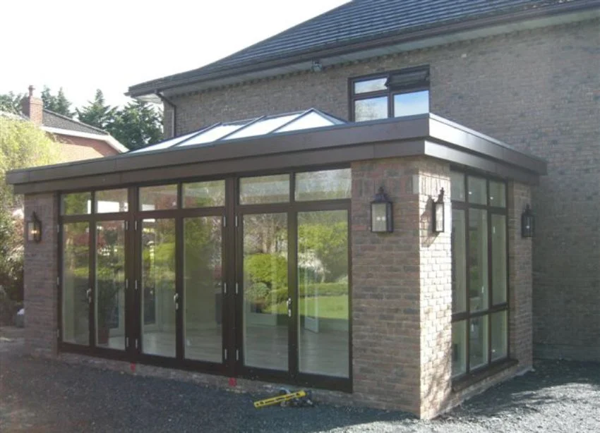 A brick and glass sunroom extension attached to a house with a sloped glass roof and sliding doors.