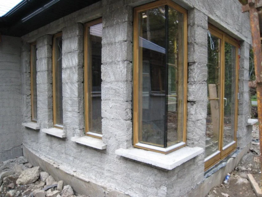 Exterior of a concrete building under construction with multiple vertical windows and wooden frames.