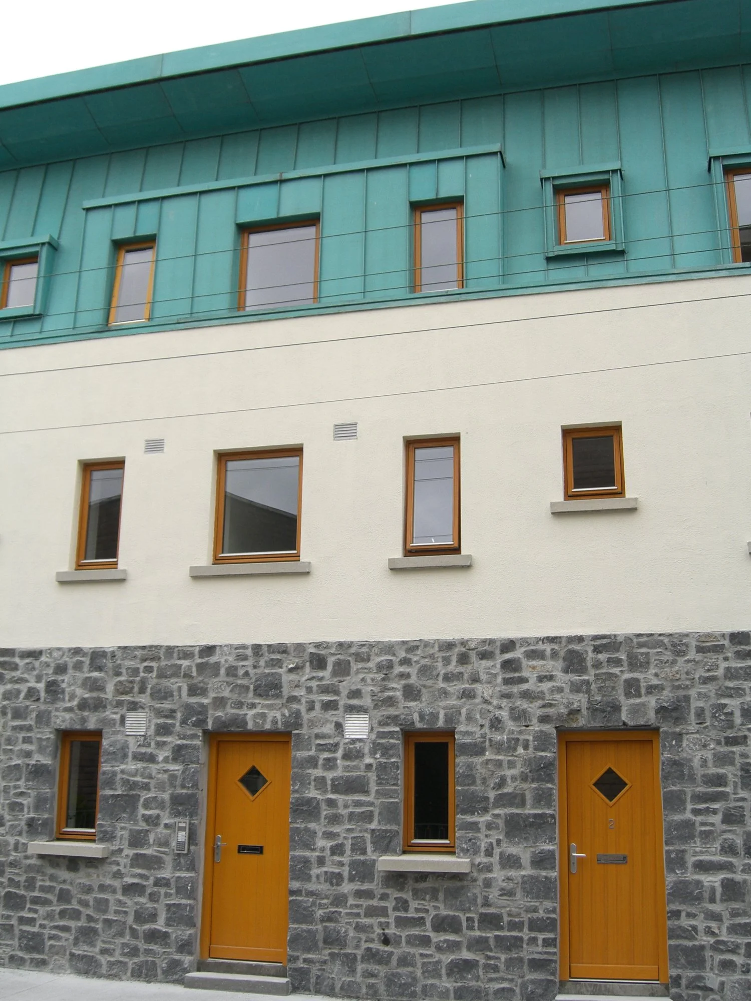 Modern building with stone facade, orange wooden doors, and teal upper section.