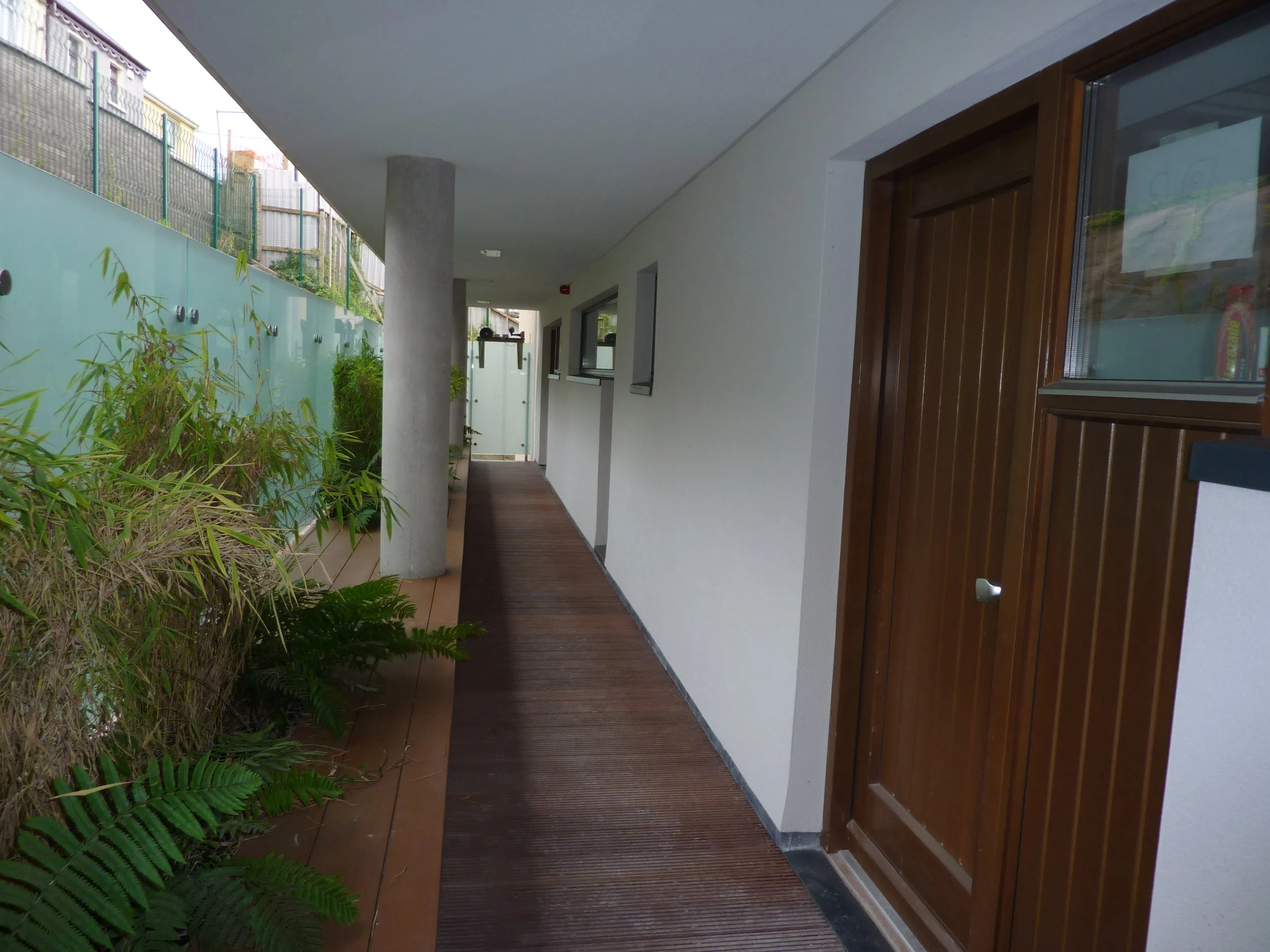 Outdoor corridor with wooden floor, plants, and glass railing
