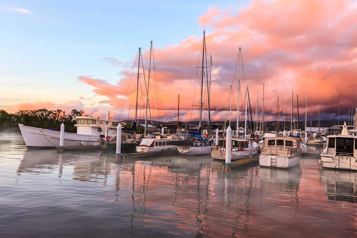 Boats docked at a Tasmanian marina during sunset with pink and purple clouds reflecting on the water.