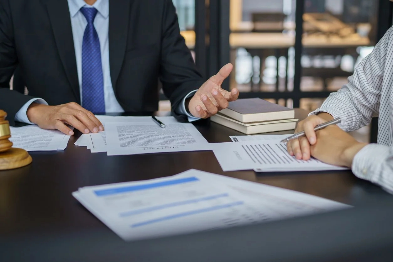 Two individuals in business attire sitting at a table with documents, discussing a contract