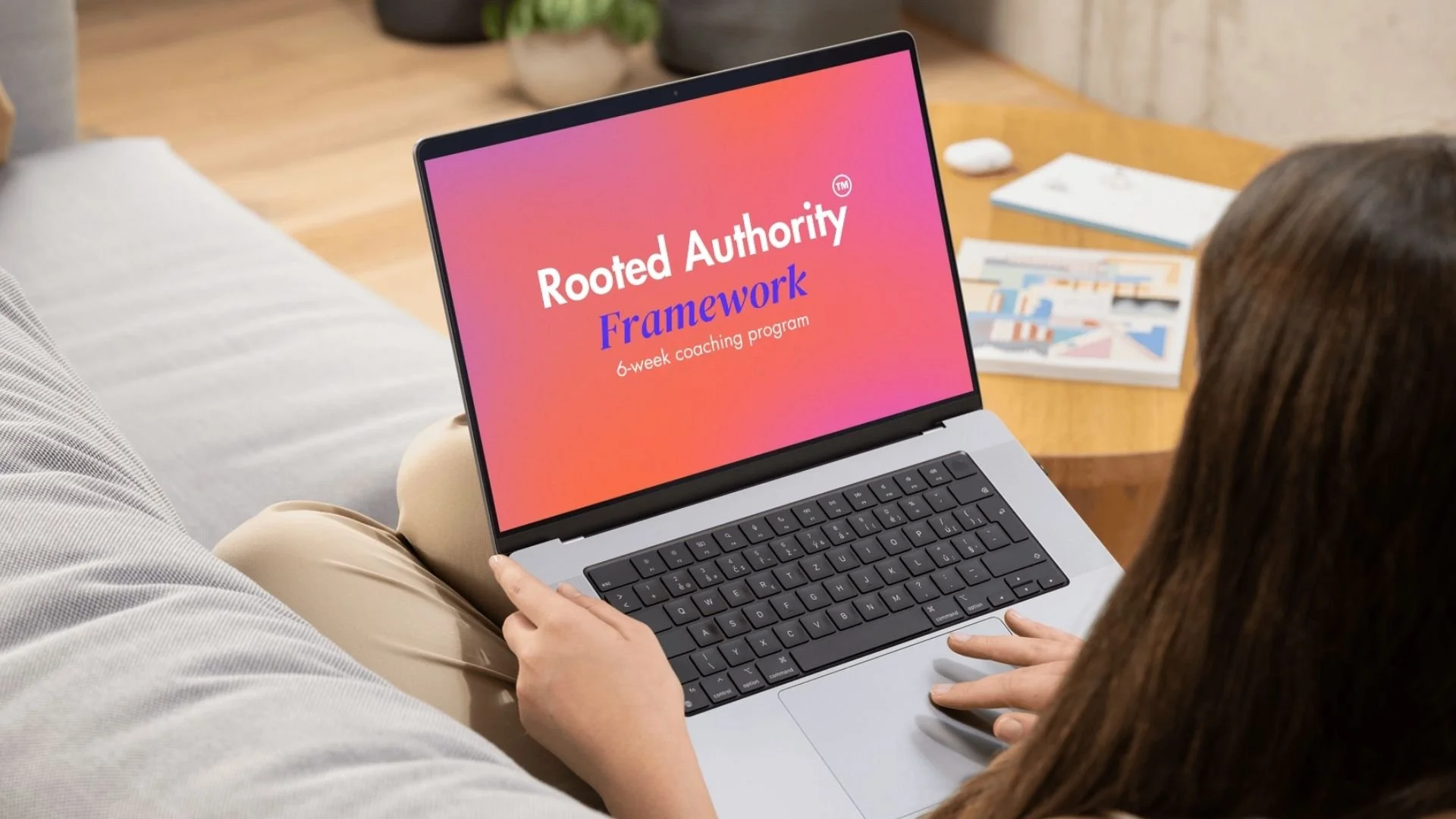 A woman sitting on a couch holding a laptop that displays a presentation titled "Rooted Authority Framework" for a 6-week coaching program.