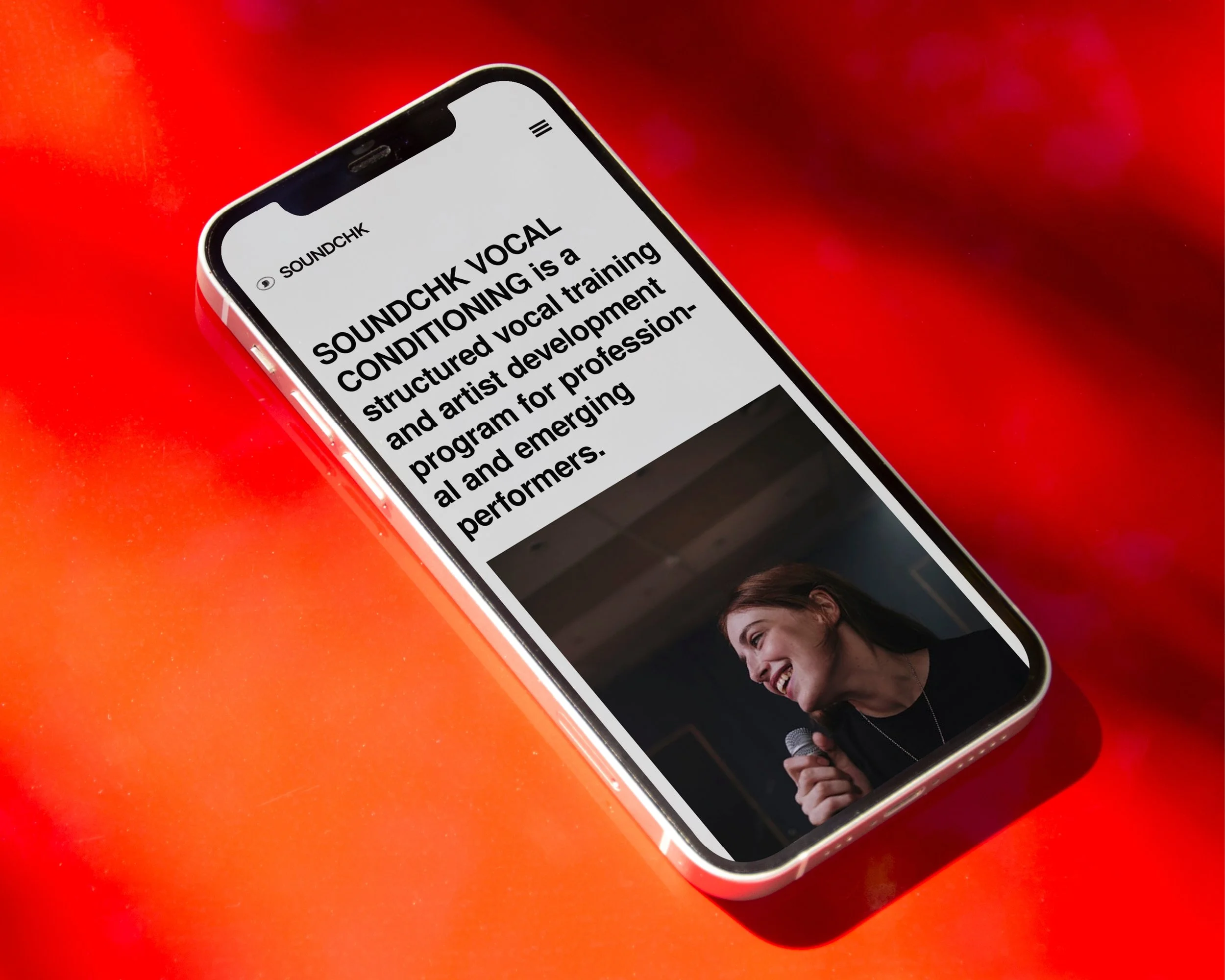 Close-up of a smartphone screen showing a website with text about SOUNDCHK VOCAL conditioning training, on a red background.