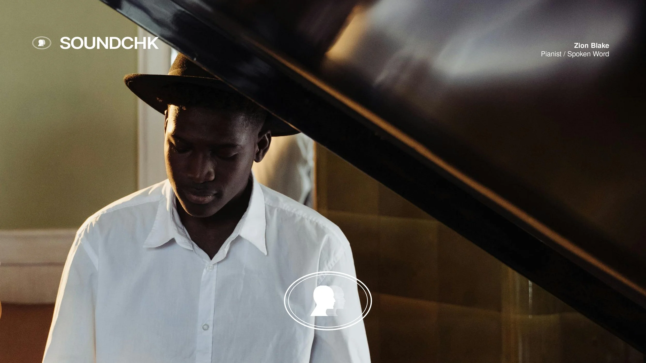 A man with dark skin wearing a white shirt and a brown hat, sitting by a grand piano with the lid open, looking down. The background shows a green wall and a window with sunlight.