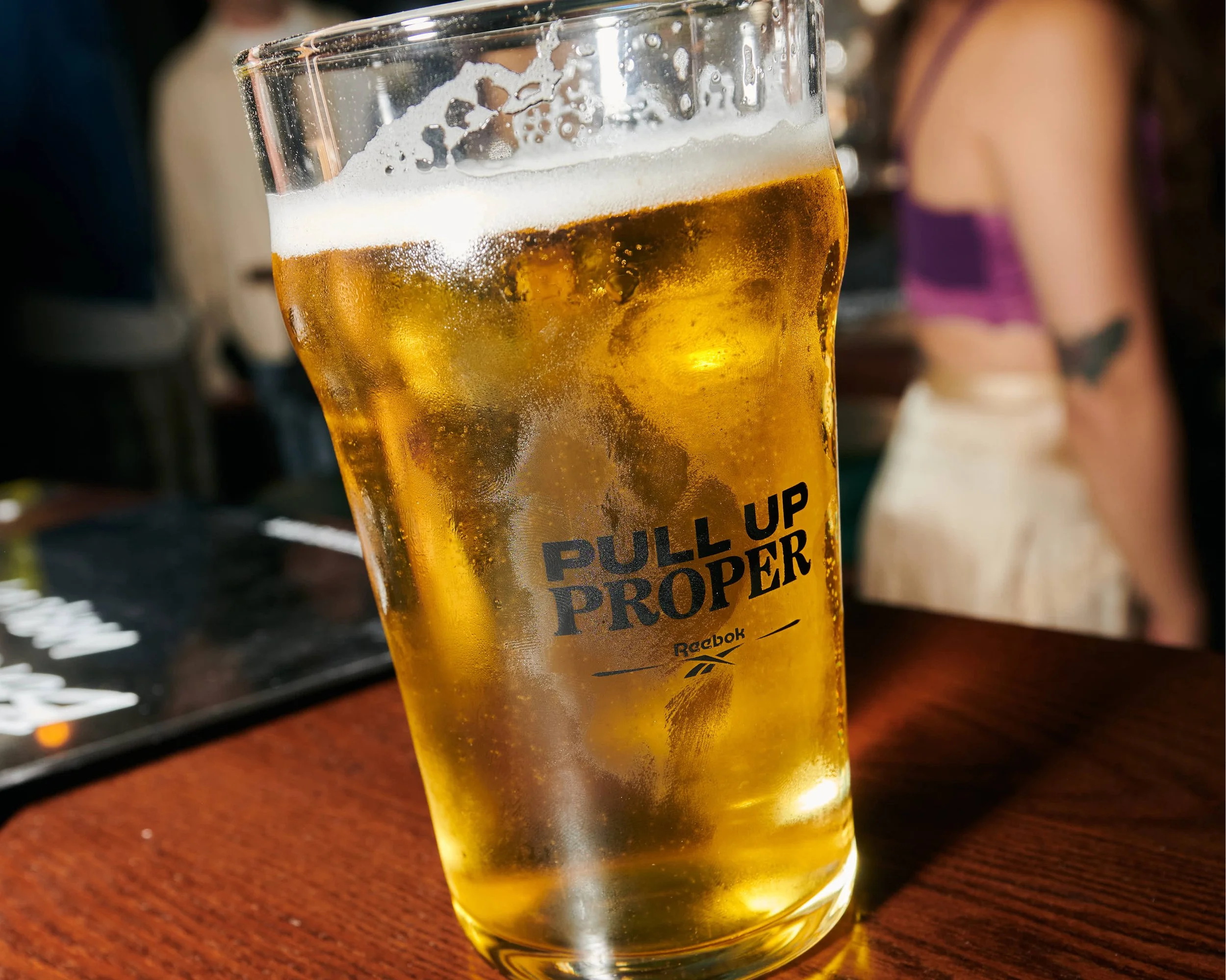 A glass of beer with foam on top, placed on a wooden surface.