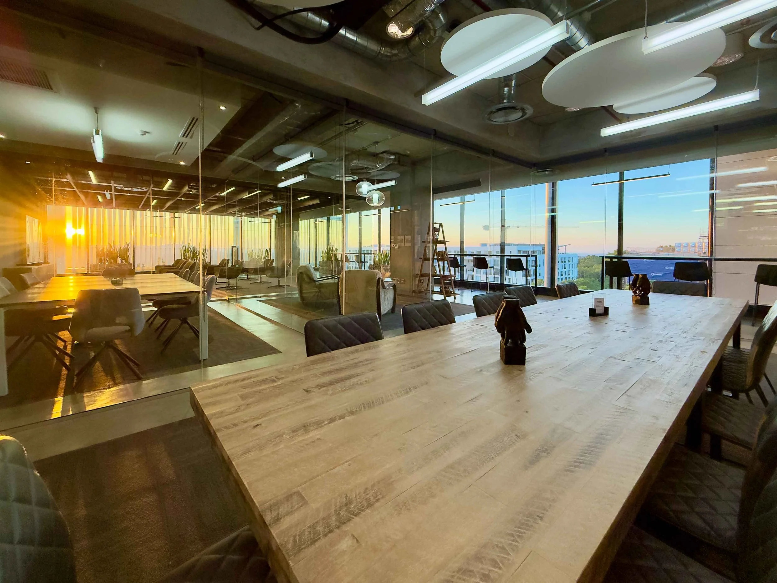 Modern conference room with a wooden table, pink chairs, large floor-to-ceiling windows, and a flat-screen TV on the white wall.