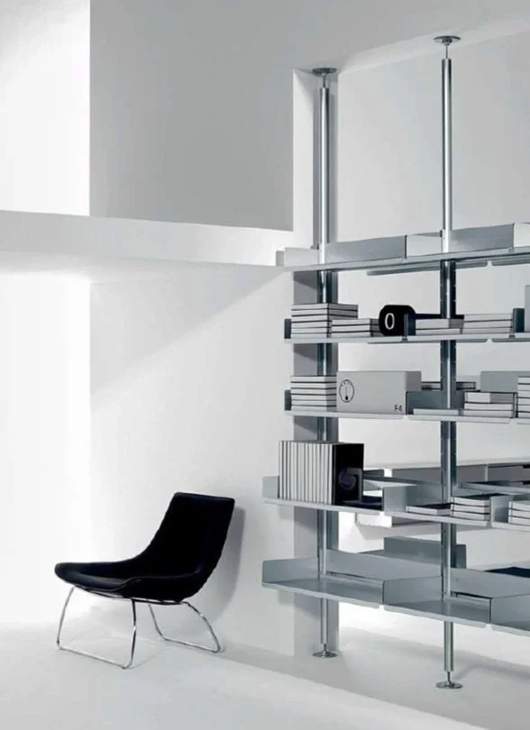 Modern black chair beside a metal and glass shelving unit in a minimalist white room.