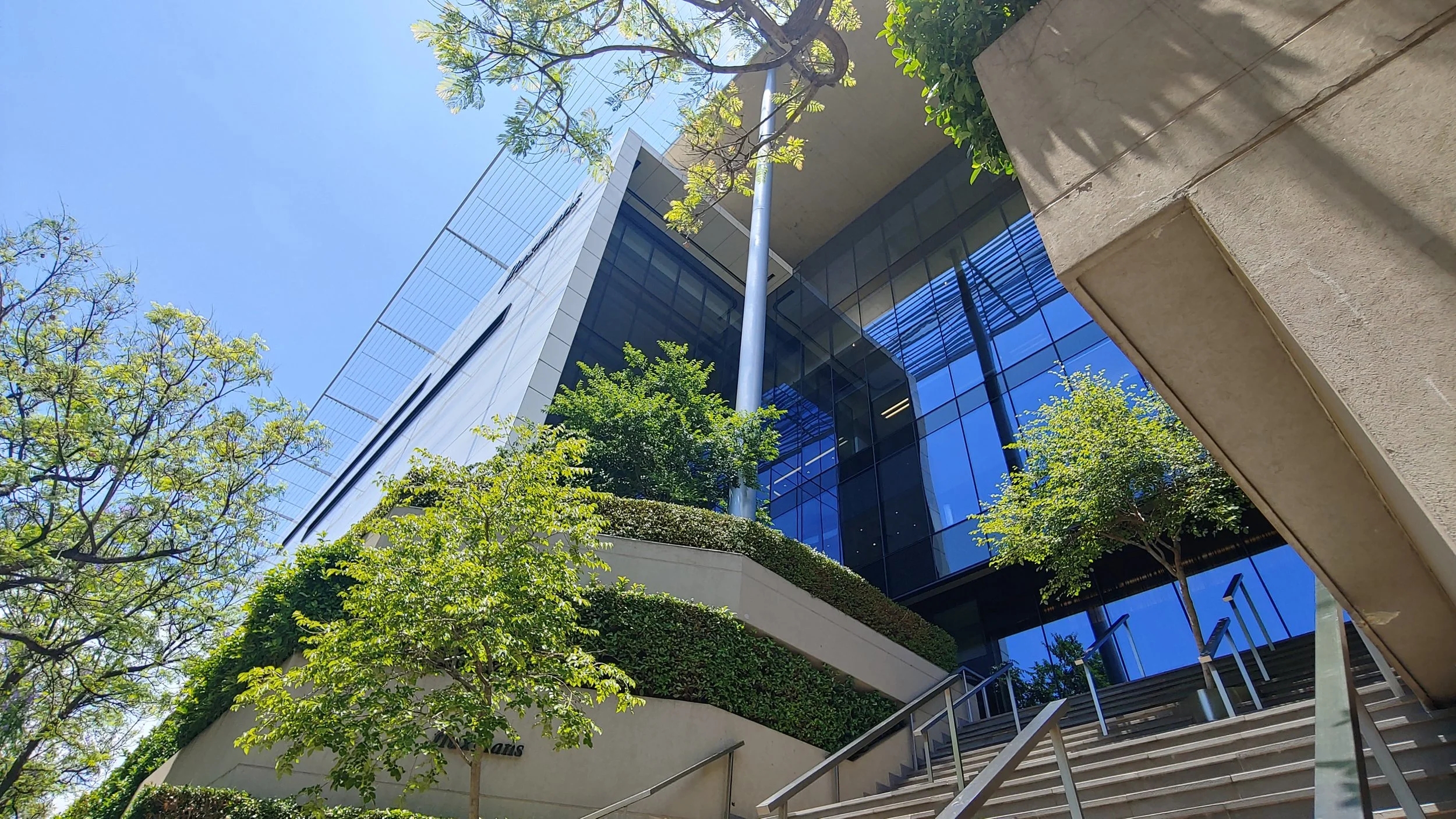 Modern glass building with greenery on a staircase, under a blue sky.