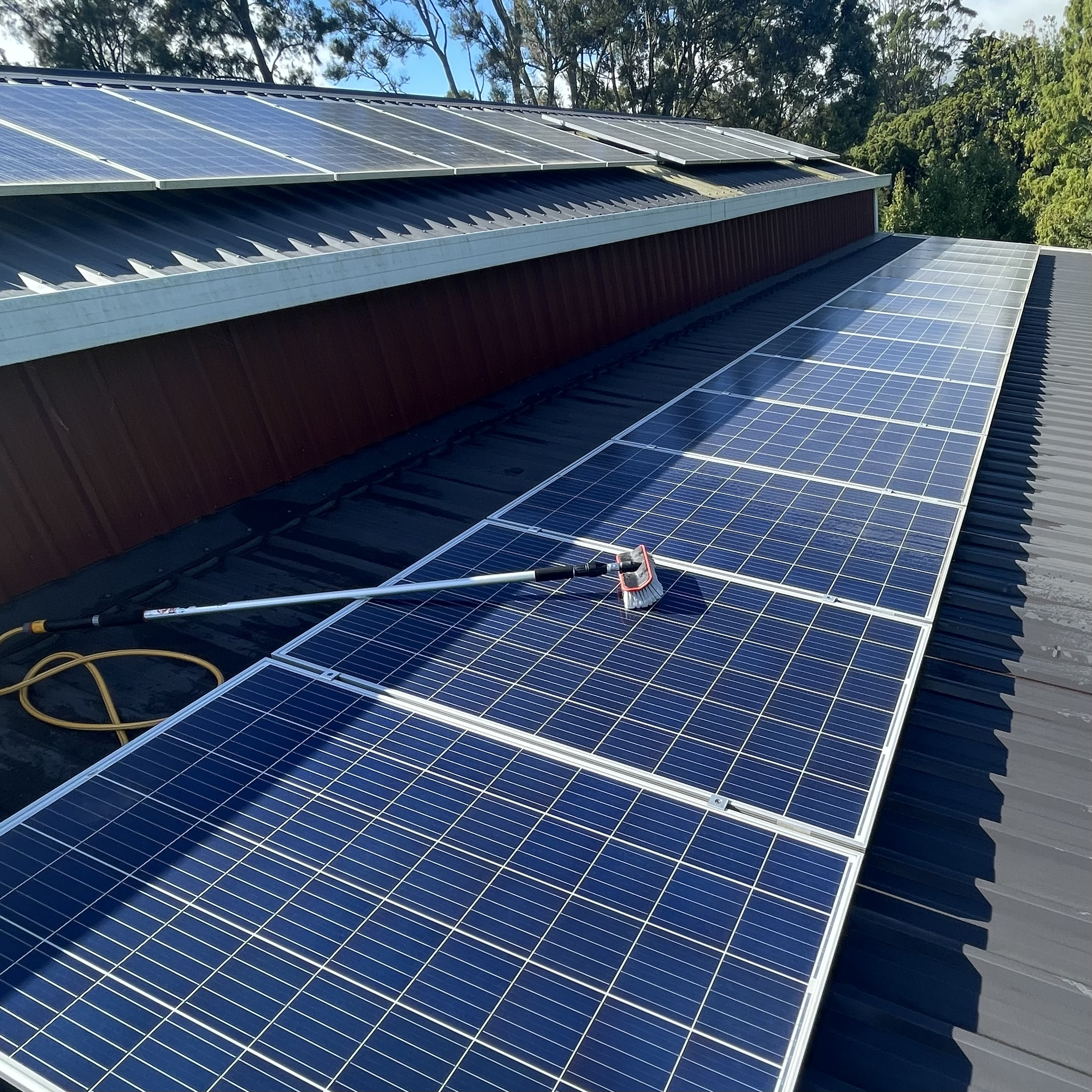 Long solar panel on a roof freshly cleaned, with a soft brush tool visible next to it, highlighting the cleaning process and reflective surface.