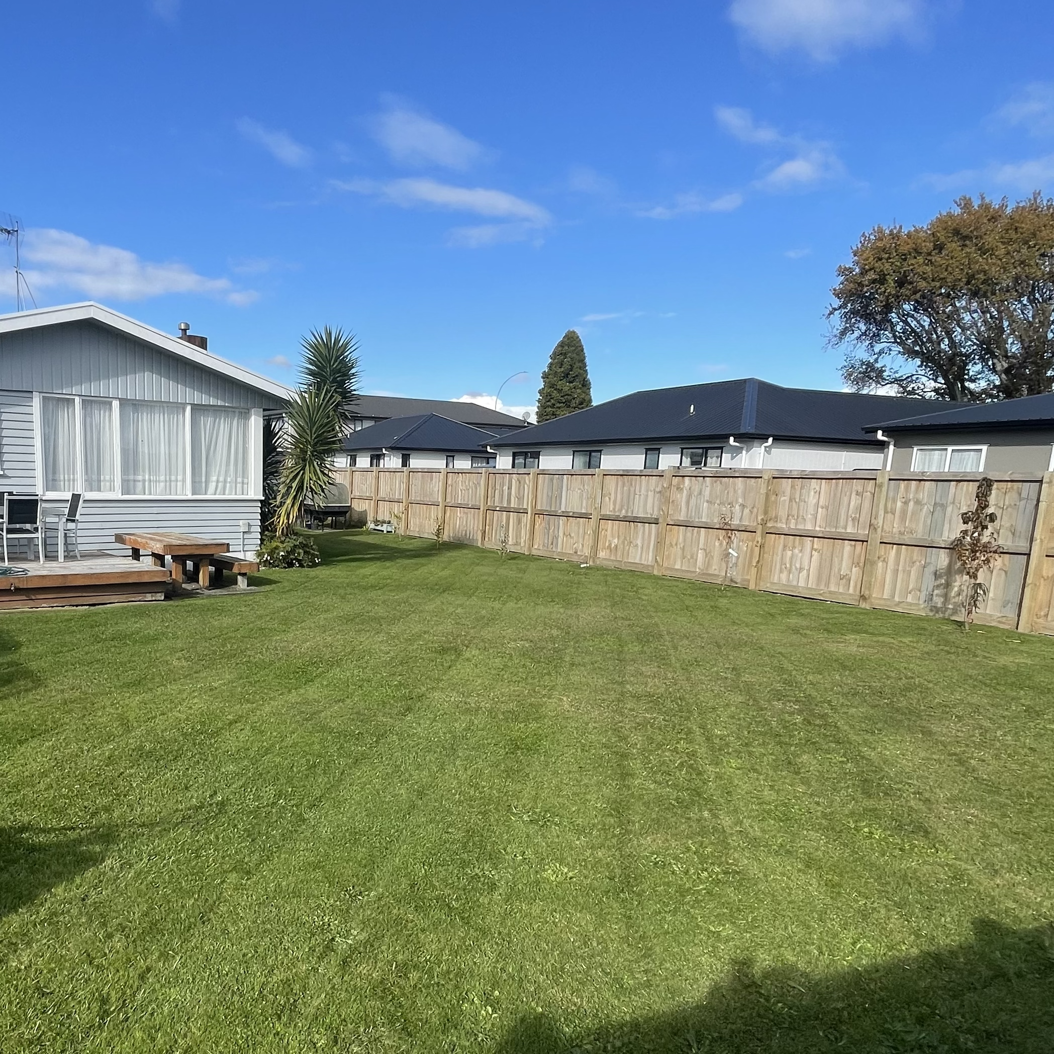 Freshly mown backyard with a visible mowing pattern, house and wooden fence in the background.