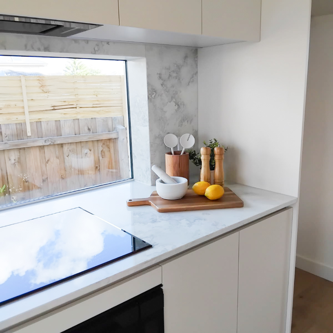Kitchen countertop with mortar and pestle, lemons, salt and pepper shakers, and utensils near a window showing an outdoor wooden fence and sky.