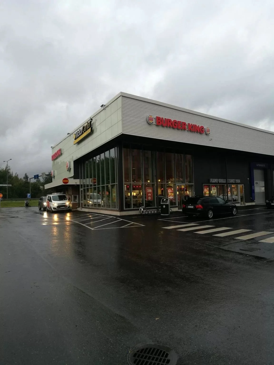 A Burger King restaurant on a cloudy, rainy day with parked cars and puddles in the parking lot.
