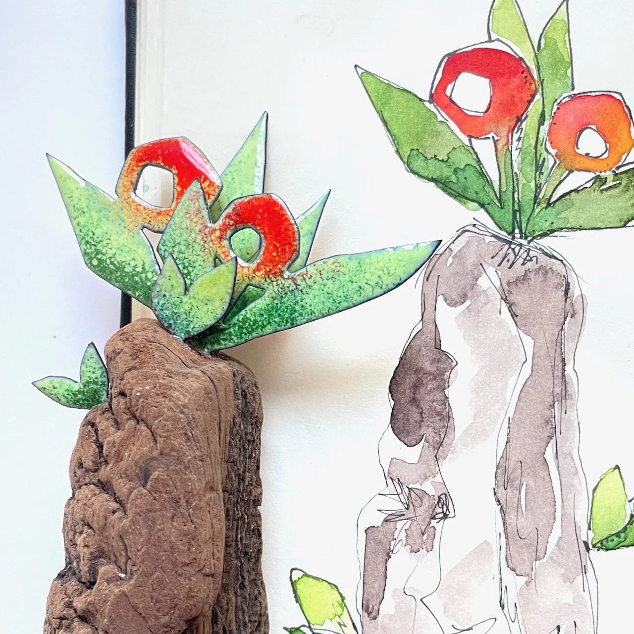 Kunstobjekt und Skizze auf einem Bild. Das Kunstobjekt heisst Rote Flora. Es ist ein Stück Treibholz, aus dem emaillierte Blätter und Blüten herauswachsen. Die Formen sind bunt emailliert, glänzen und haben dunkle Umrisslinien.