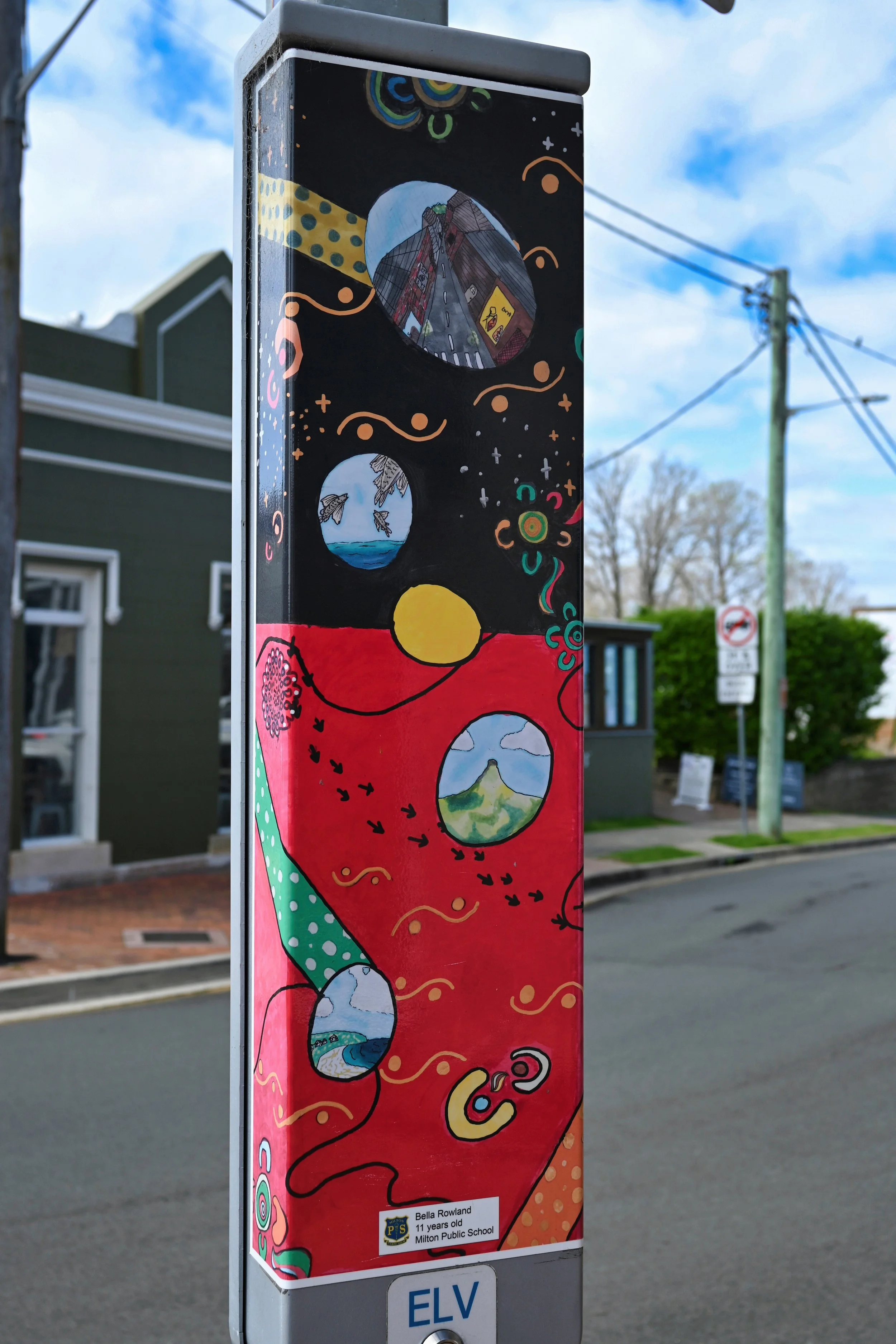 Colorful mural art on a street sign depicting various scenic landscapes, with a label indicating it was created by Bella Rowland, an 11-year-old student at Milton Public School.