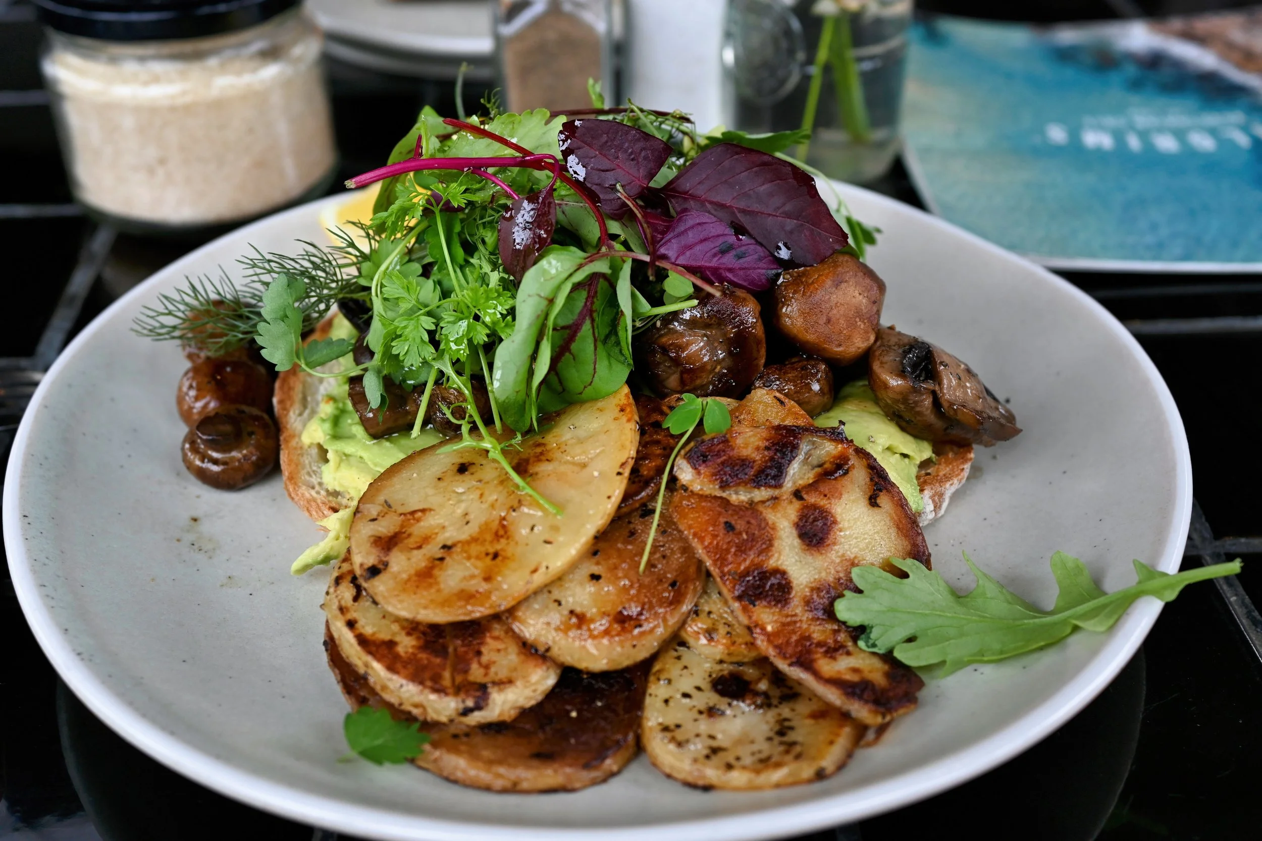 A white plate with grilled potato slices, sautéed mushrooms, guacamole, and mixed fresh greens including purple and green leaves.