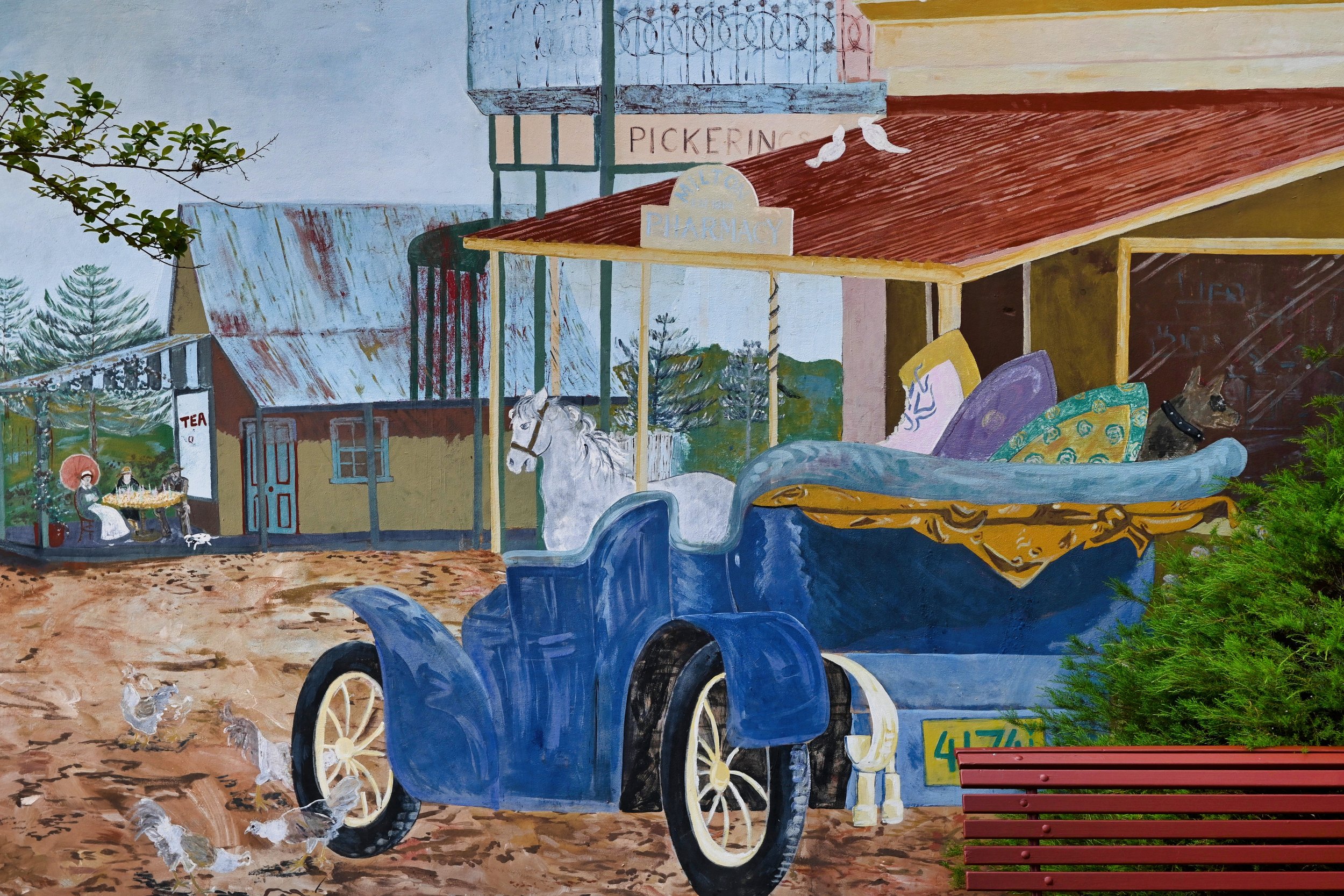 Colorful mural of a vintage blue car with a horse in the carriage, parked in a countryside village with trees, a small building, a bench, and chickens pecking on the ground.