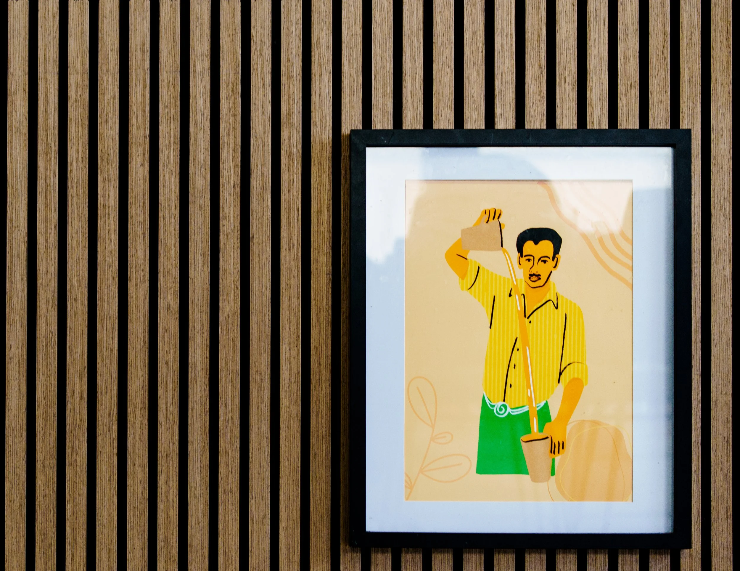 Framed colorful illustration of a man with dark hair, wearing a yellow striped shirt and green pants, planting a seed in a small pot. The background features abstract shapes and leaves.