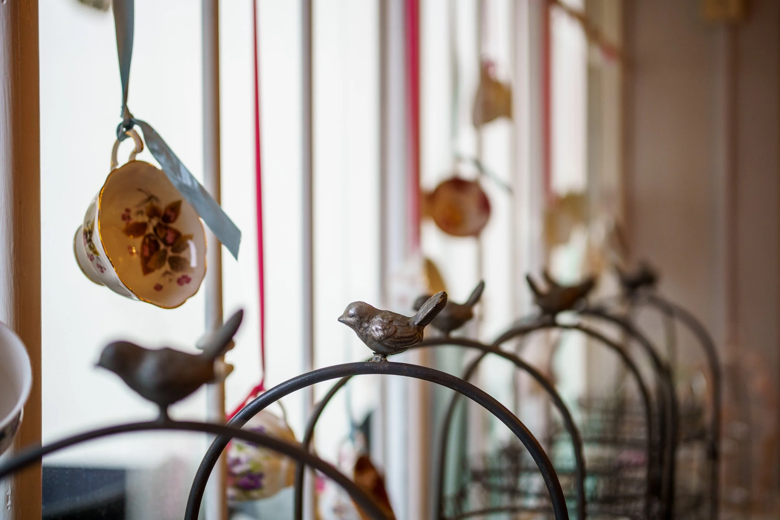 Decorative metal birds on a wire with ceramic hearts hanging behind them, indoors with sunlight streaming through a window.