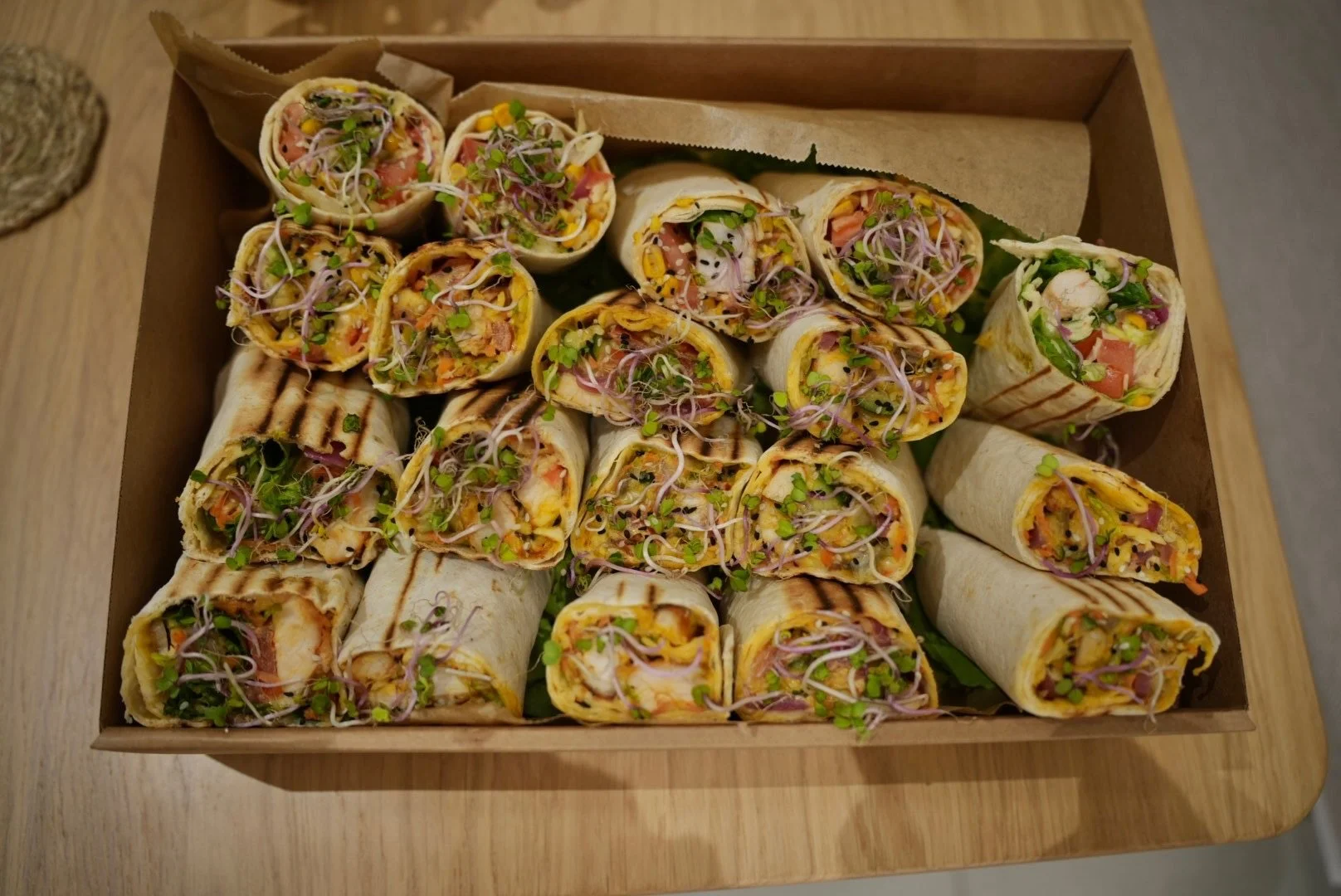 Verschiedene Wraps mit Gemüse, Fleisch und Sprossen in einer Pappschachtel auf einem Holztisch.