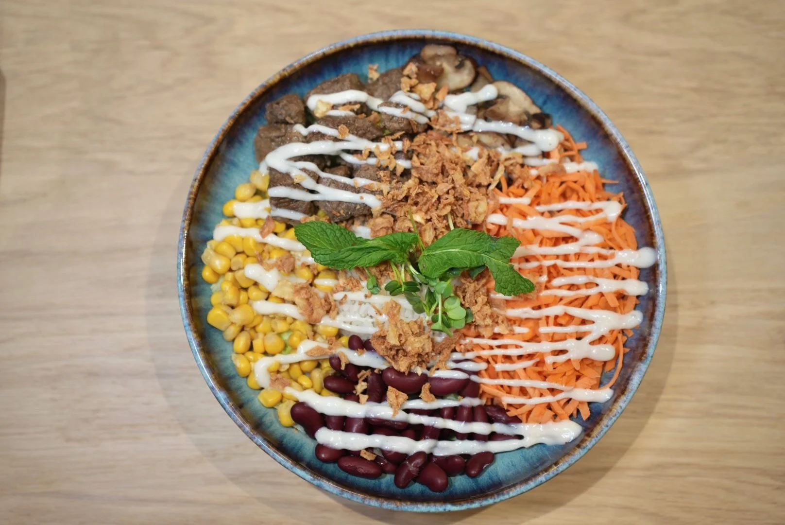 Buddha-Bowl mit Mais, schwarzen Bohnen, geraspelten Karotten, gebratenem Fleisch, Zwiebeln, Kräutern und einer cremigen Sauce