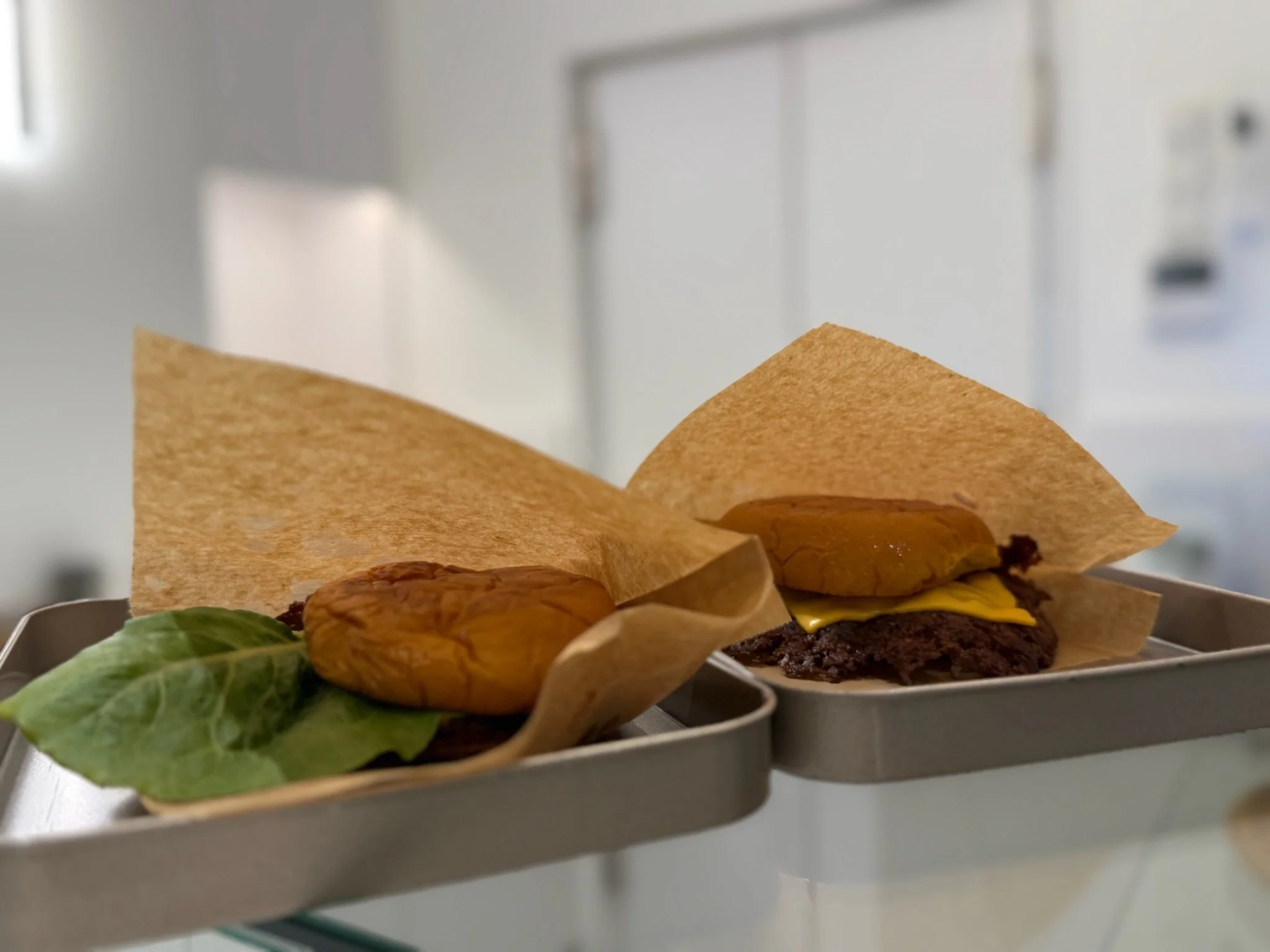 Zwei Hamburger Patties mit Käse, Salat, in Backpapier eingewickelt, auf Metallplatten