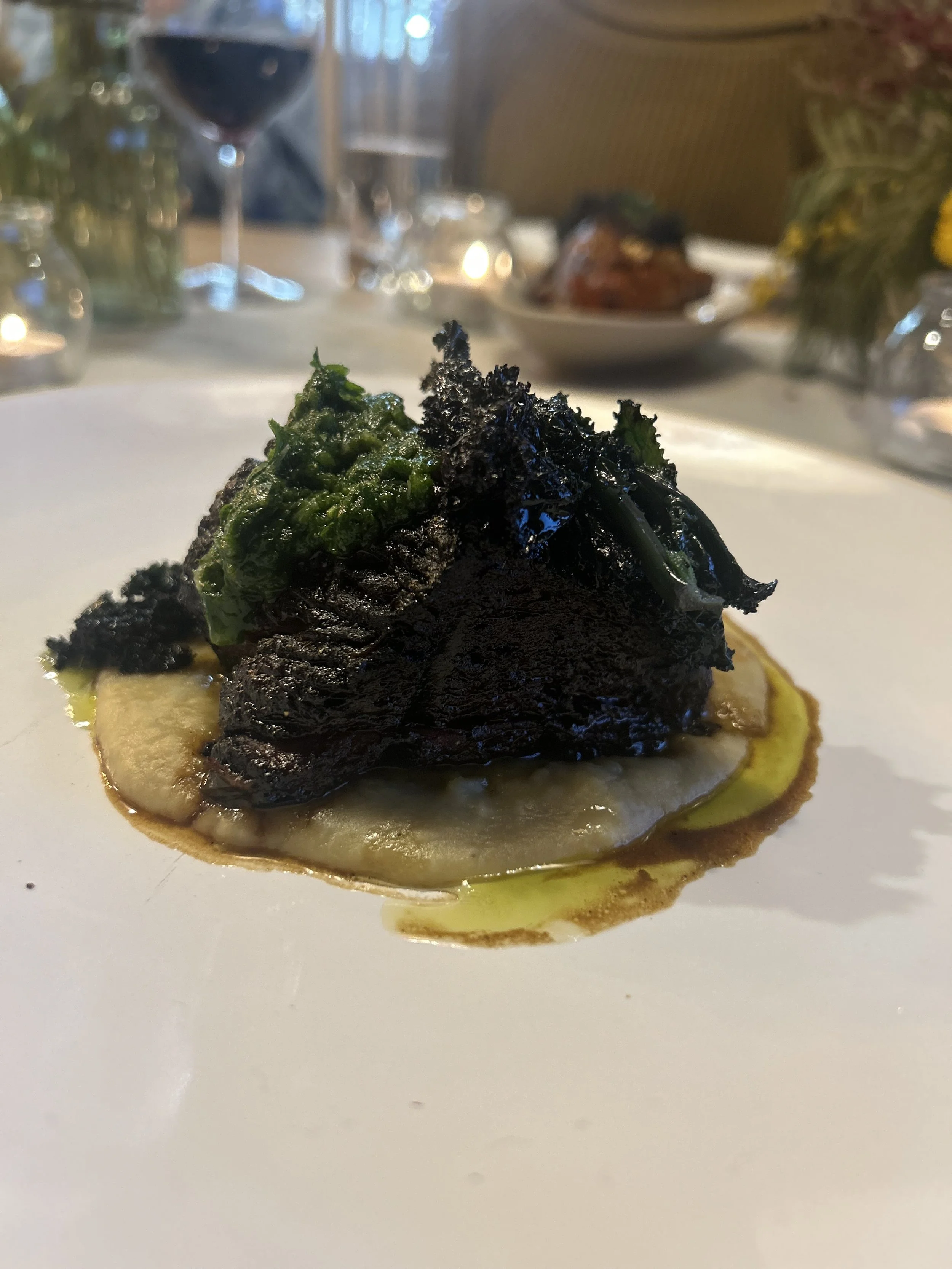 Gourmet dish with greens and sauce on a white plate, wine in background.