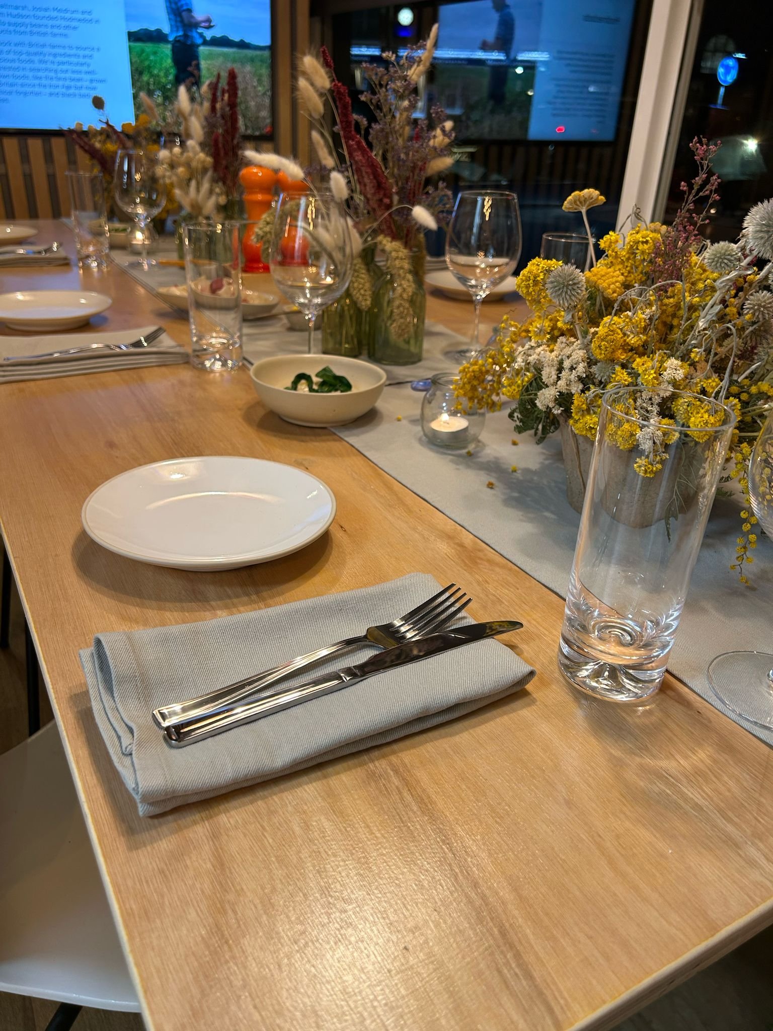 Table setting with plates, glasses, cutlery, and decorative dried flowers on a wooden surface.