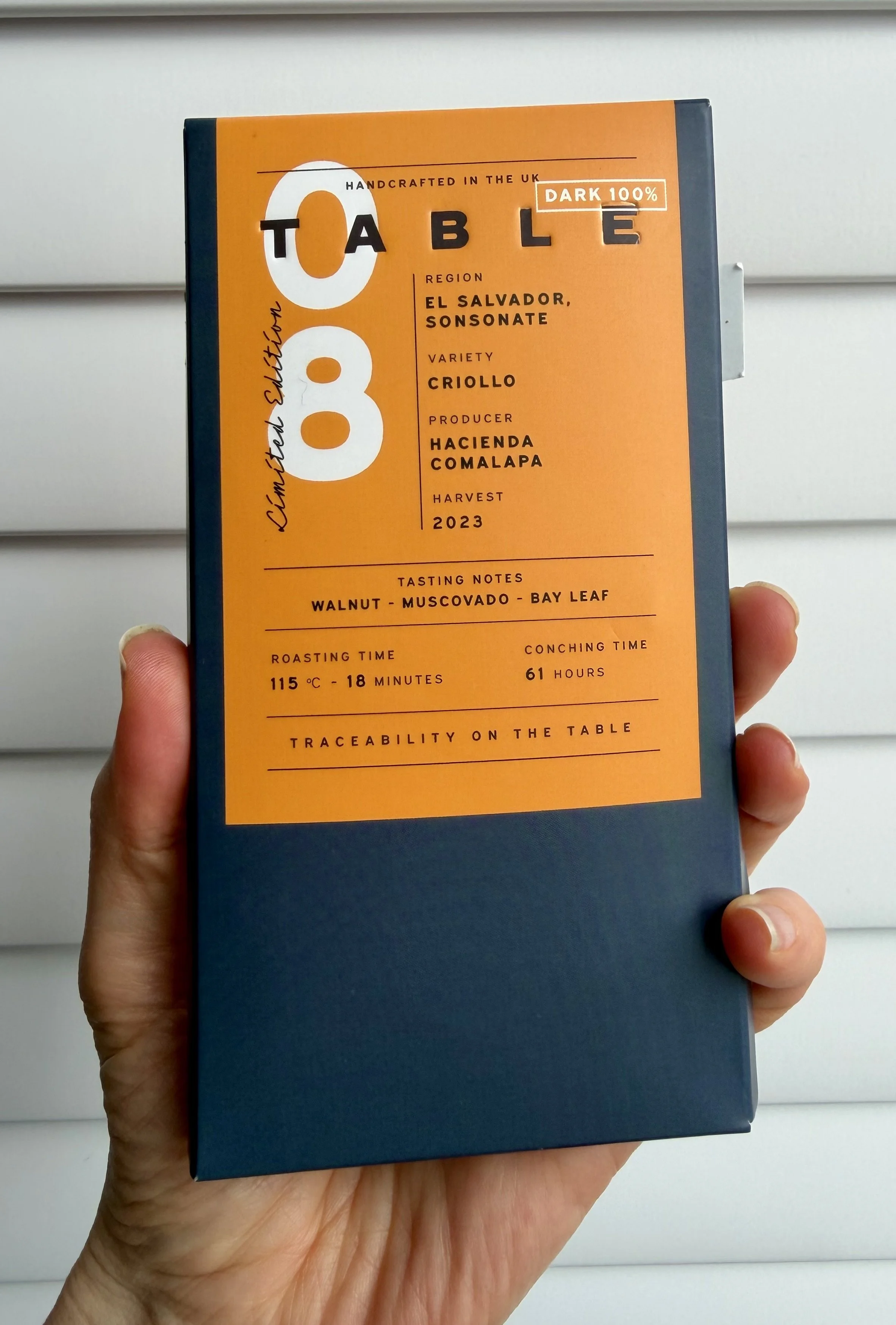 Navy and orange packaging of Table chocolate 100% bar being held up.