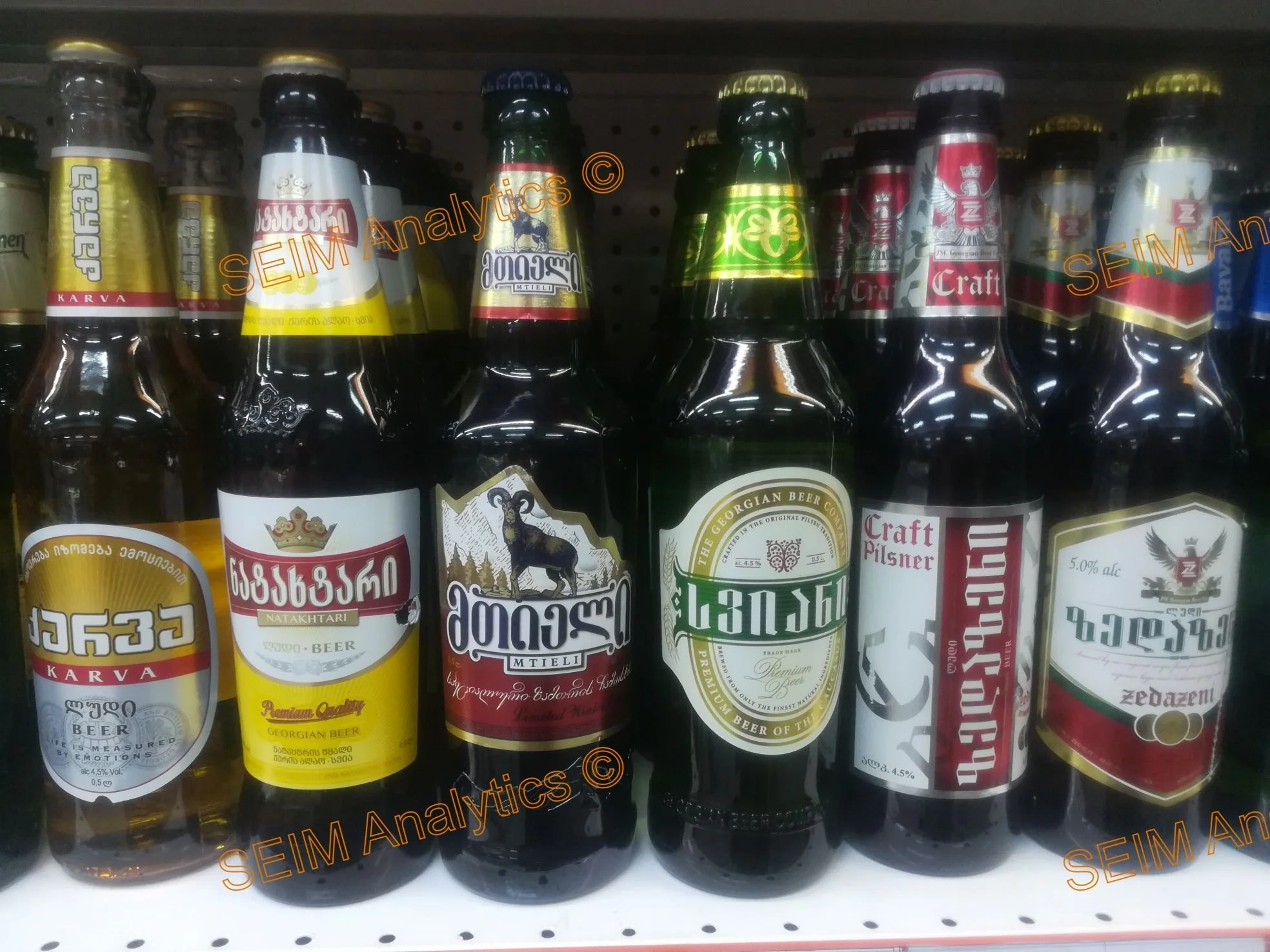 A shelf of various beer bottles with labels in Georgian script and English, including Karva, Natakhtari, Mtel, Georgian Beer, Craft Pilsner, and Zedazeni varieties.