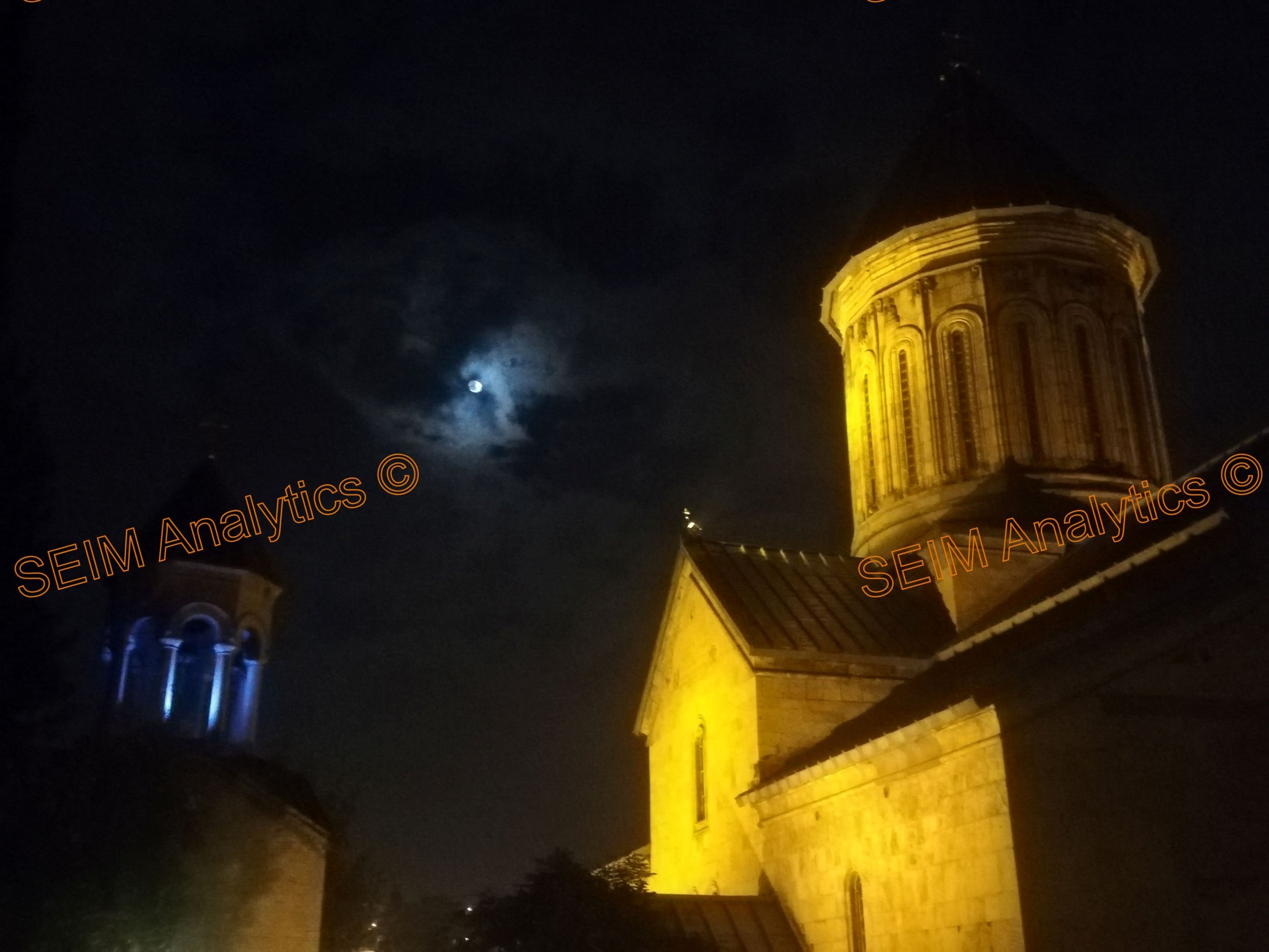 Night-time view of a historic church in downtown Tbilisi, Georgia with illuminated stone walls and a bright moon.