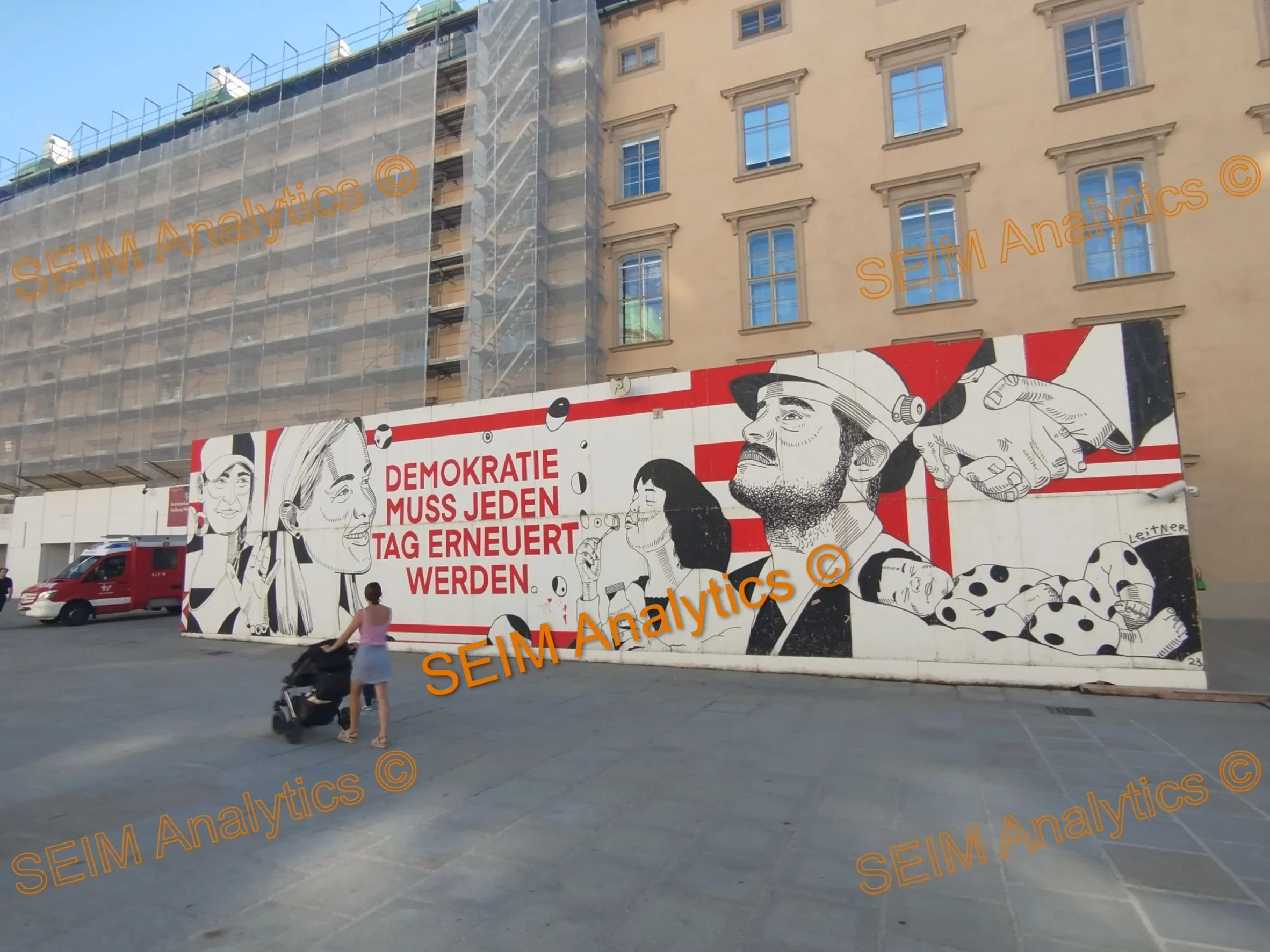 A mural with black and white illustrations of people, including a woman, a man wearing a hat, and others, with red accents, featuring German text that reads 'Demokratie muss jeden Tag erneuert werden.' The mural is on a construction wall in an urban setting.