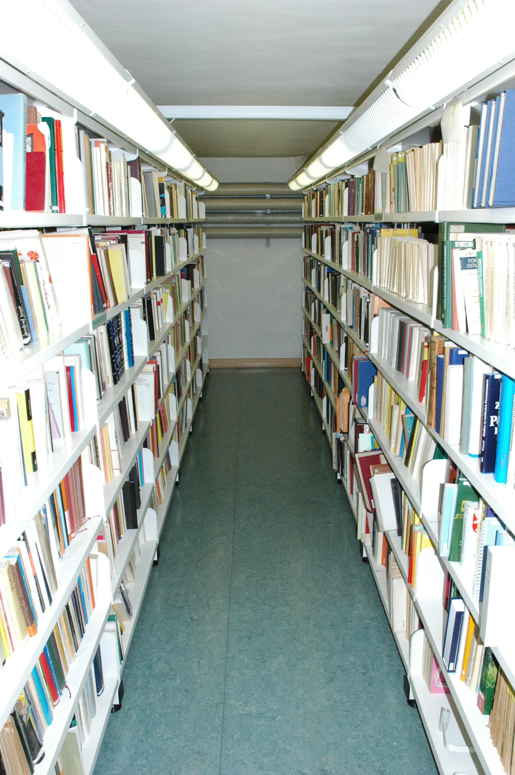 A narrow aisle in a library with tall bookshelves filled with books on both sides.
