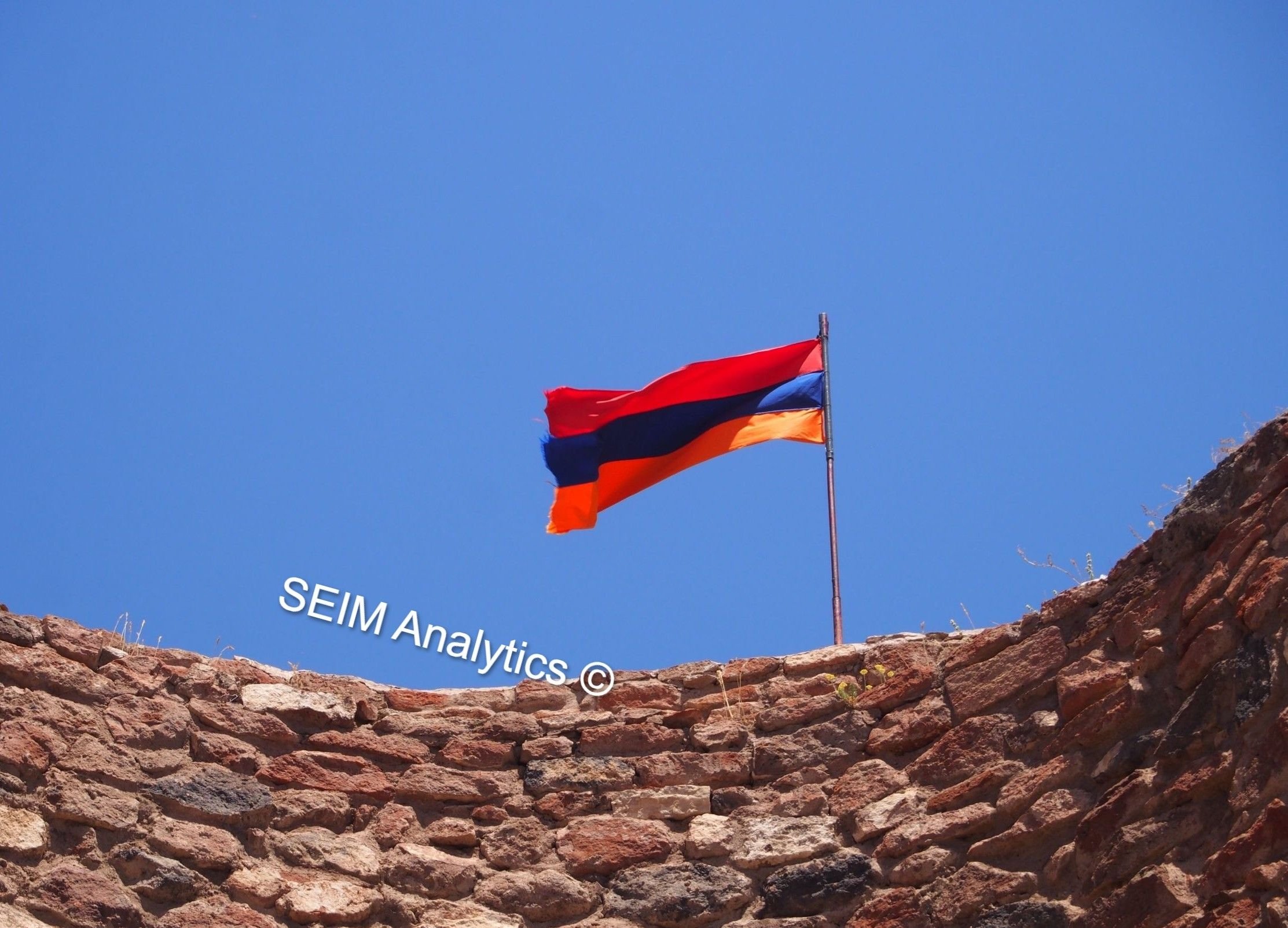 Armenian flag with red, blue, and orange stripes flying atop a stone wall at a monastery in Aragatsotn Province (Talin area).