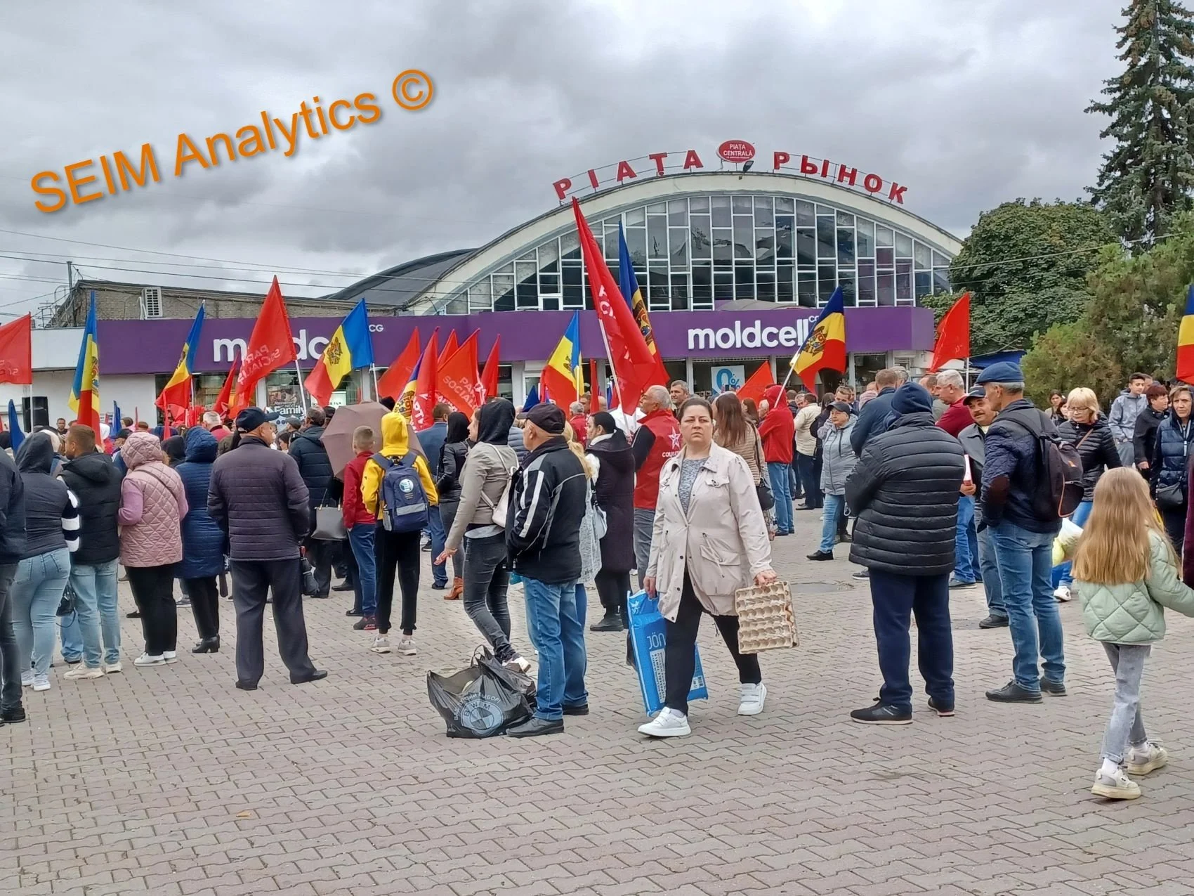 Crowd of people gathered outside a building with signs and flags, including Romanian flags, during a protest or demonstration.