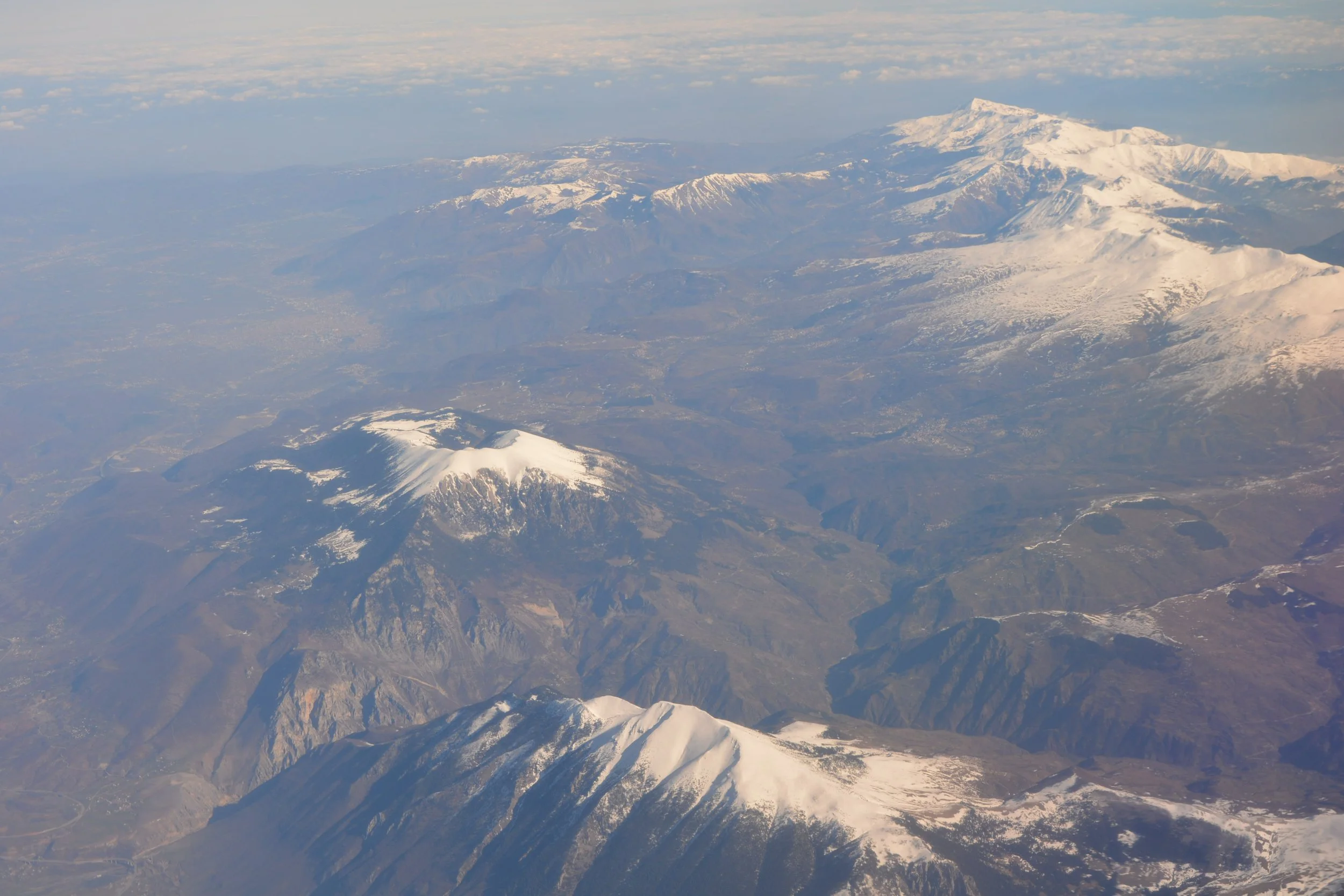 Aerial view of snow-capped mountains with rugged terrain and clear sky.