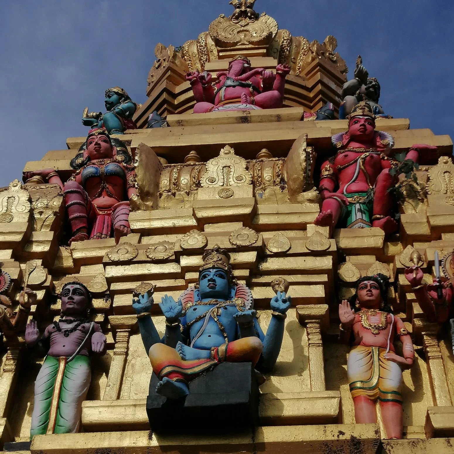 Close-up of a colorful Hindu temple tower with multiple painted deity sculptures against a blue sky.