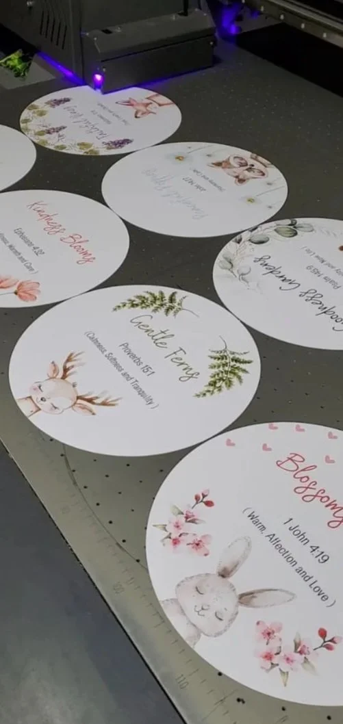 Round paper signs with floral and animal illustrations, displaying names, Bible verses, and messages, likely for a wedding or celebration event.