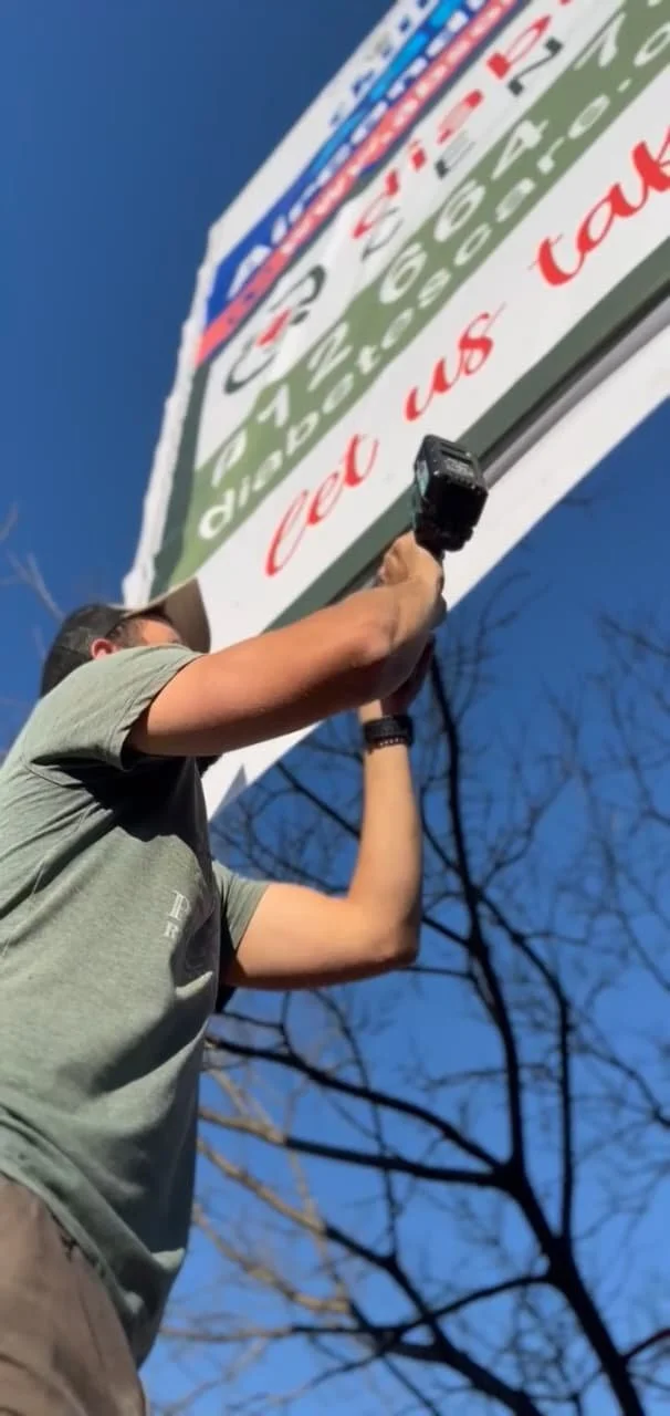 A person installing a large sign on a building during daytime.