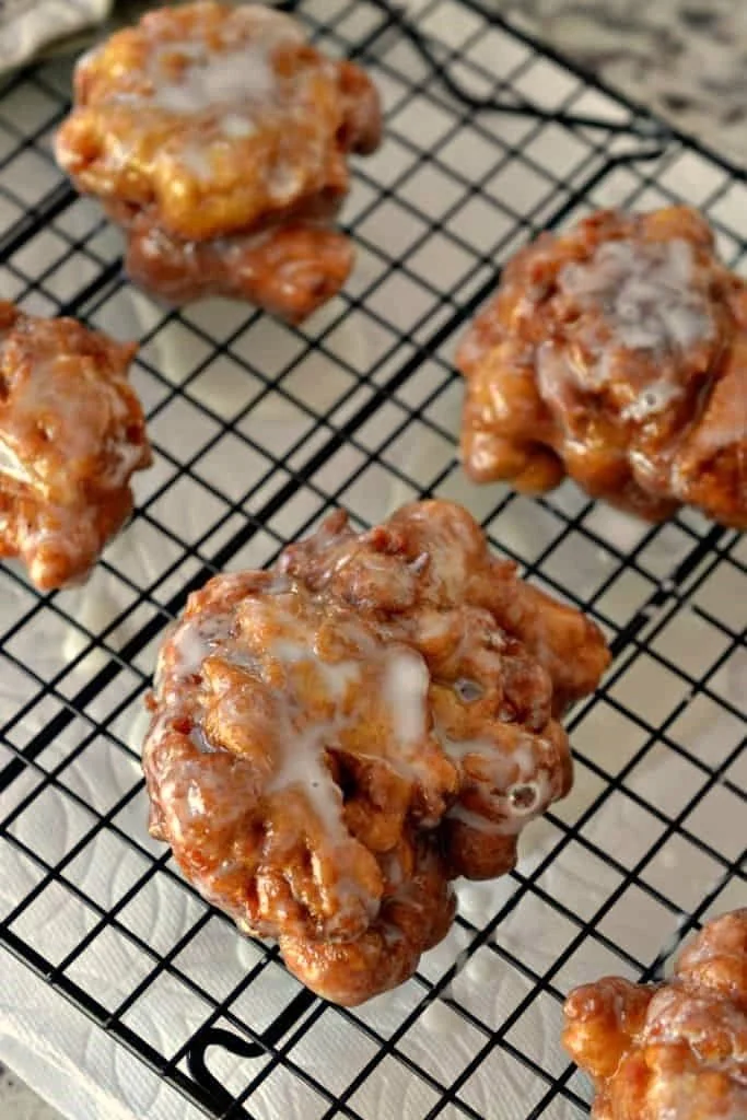 four apple fritters on a wire cooling rack, freshly fried and dipped in a sugar glaze