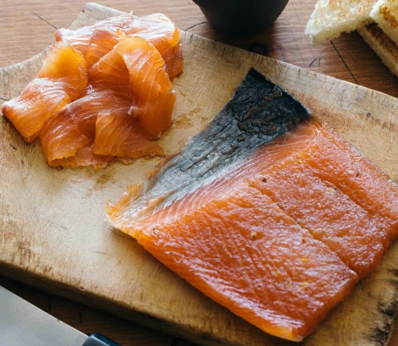 Thinly sliced homemade gravlax with a vibrant orange color, garnished with fresh dill and lemon slices.
