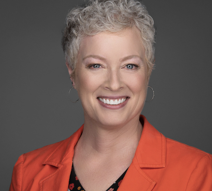 Headshot of a professional woman with short gray hair wearing a red suit jacket