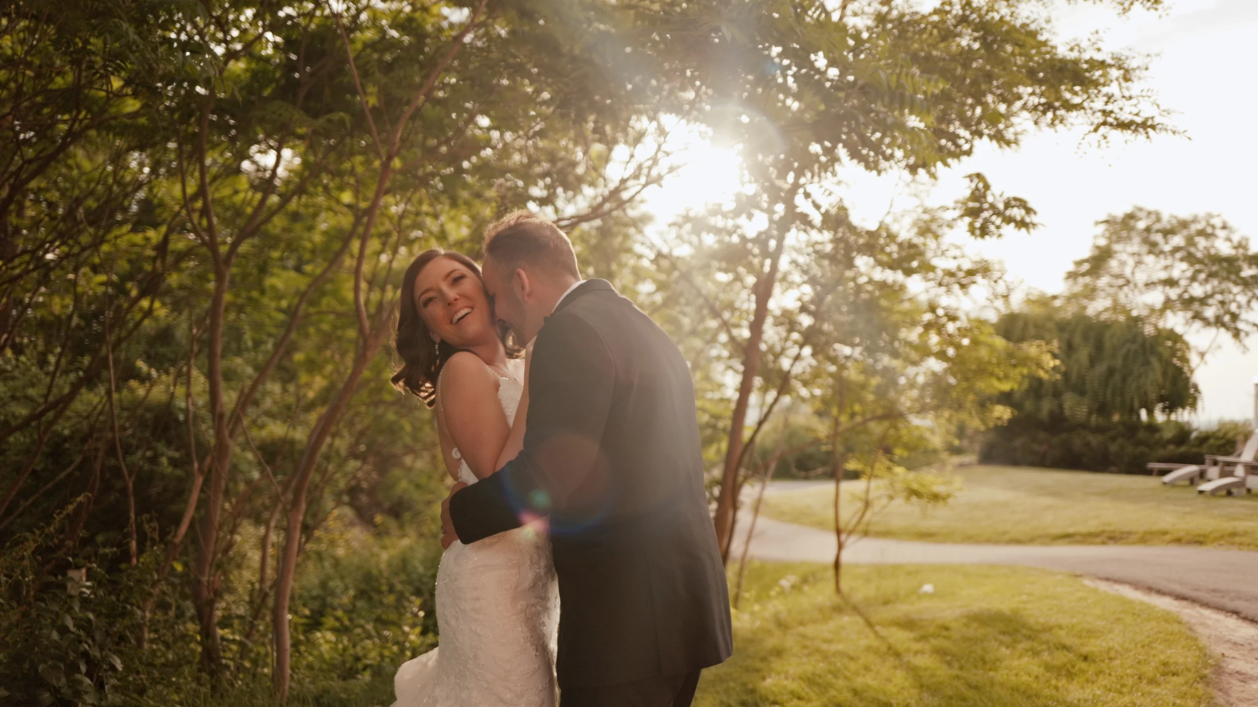 Bride and groom laughing and embracing in a sunlit outdoor park setting.