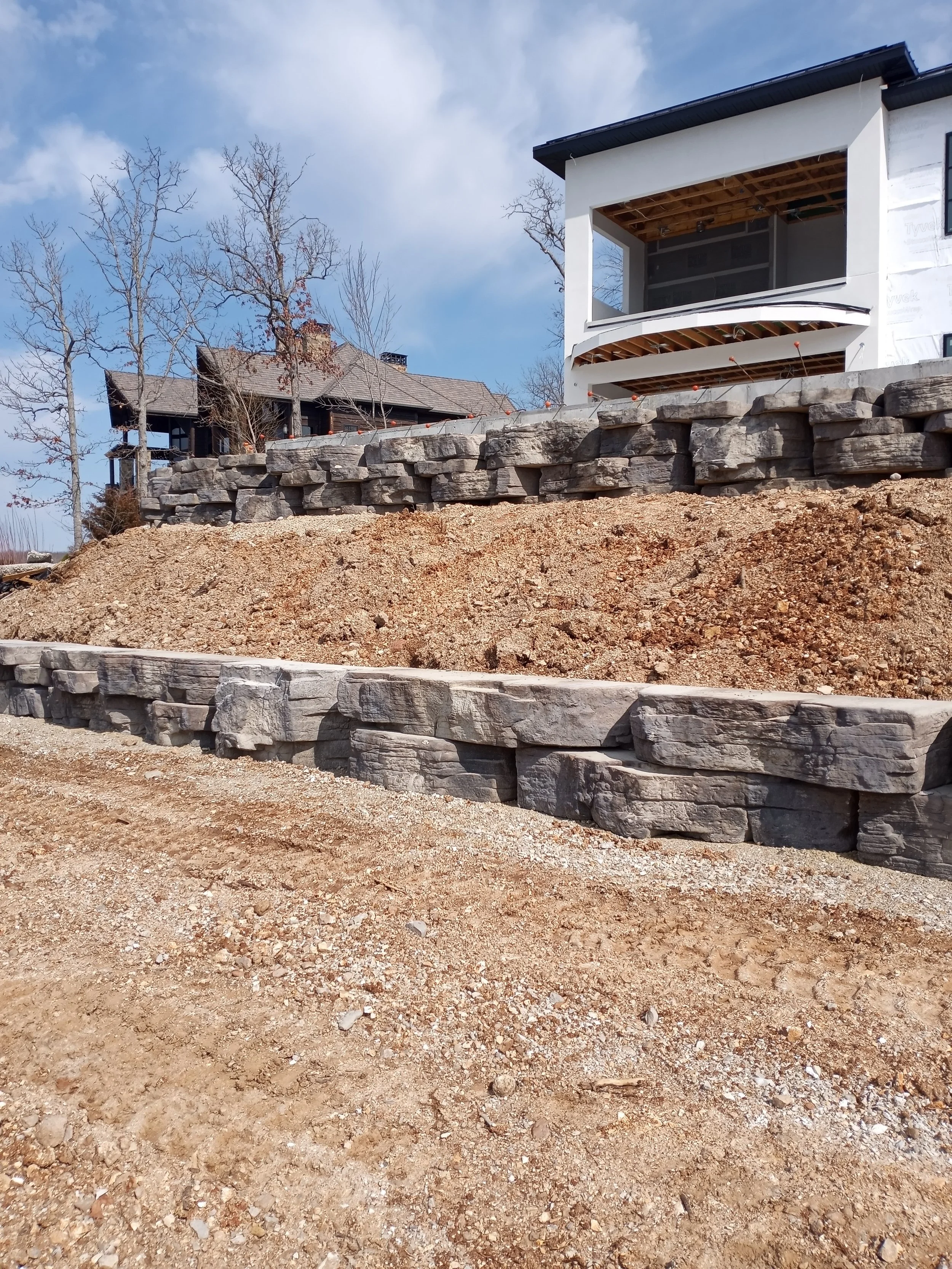 A construction site with stacked rocks and dirt in front of a house that is under renovation, with a partially completed exterior wall.