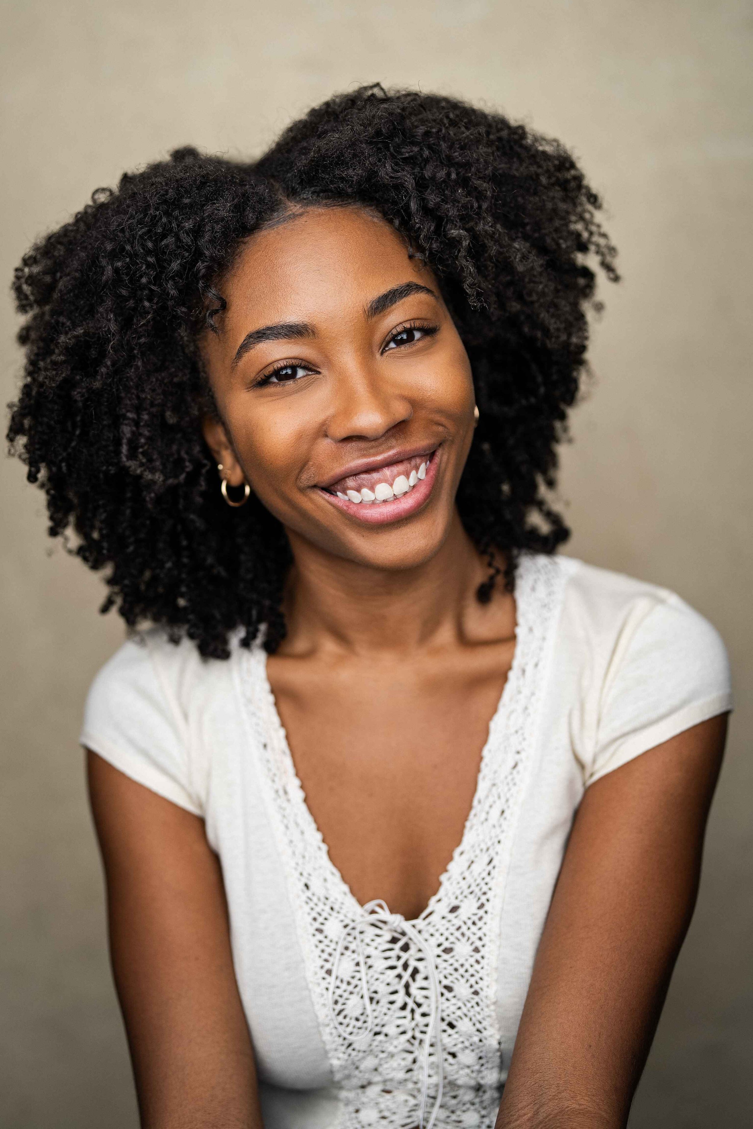 Actor Nicole Stewart smiling with curly hair wearing a white top
